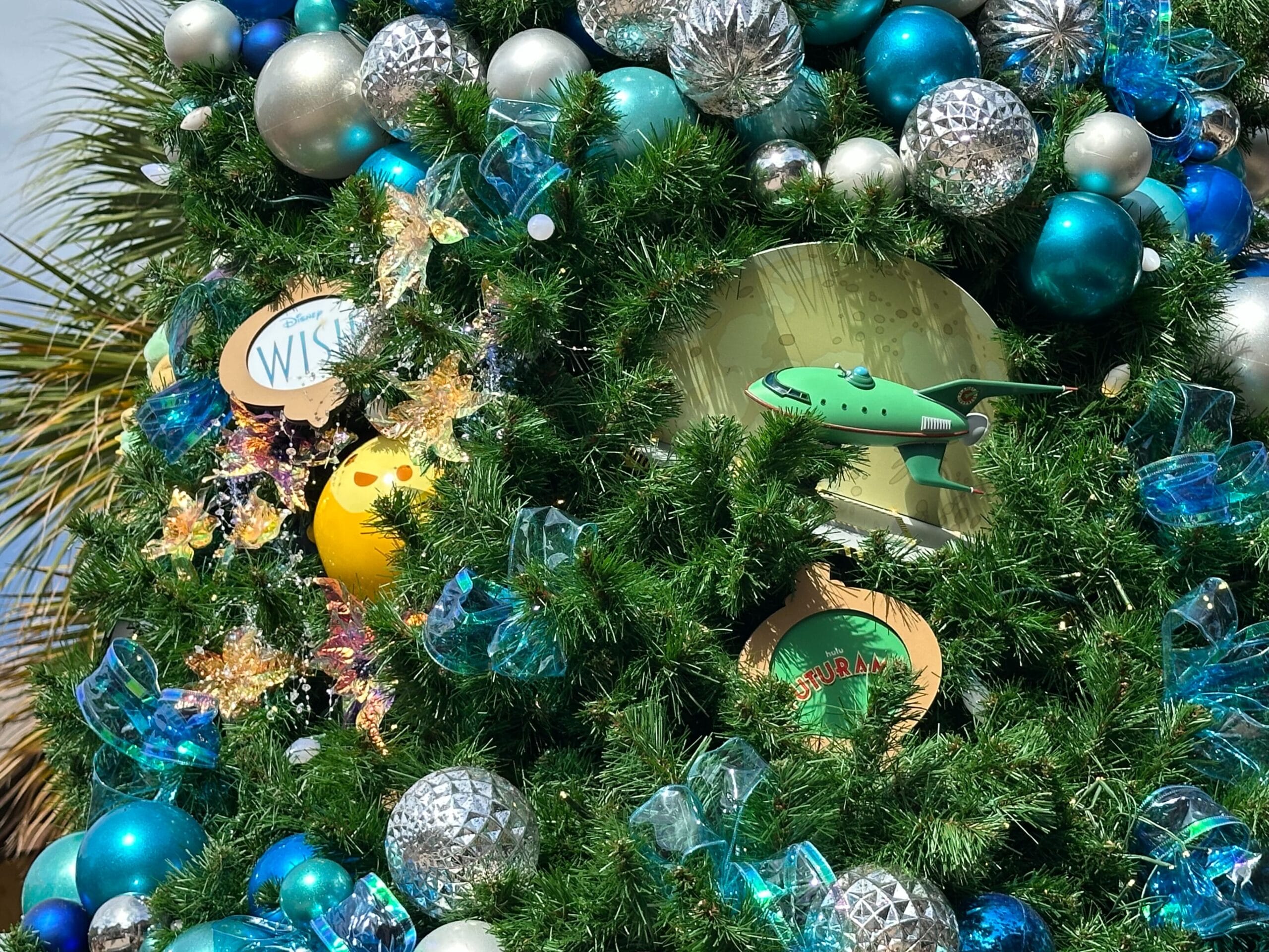 Close-up of a decorated Christmas tree featuring green and silver ornaments, a small model airplane, and a round plaque.