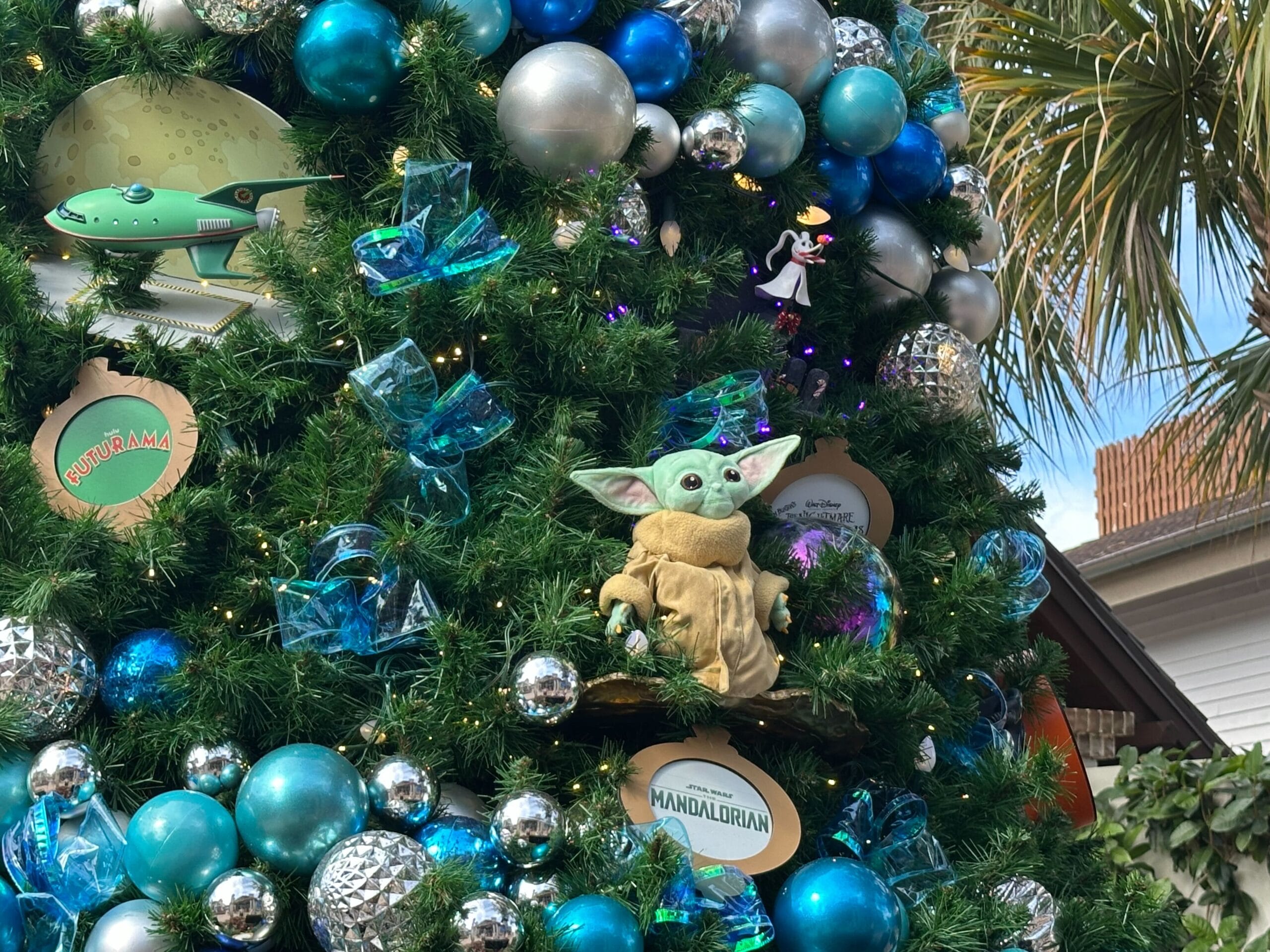 Christmas tree decorated with blue and silver ornaments, featuring a green Yoda character and themed trinkets. Palm tree in the background.