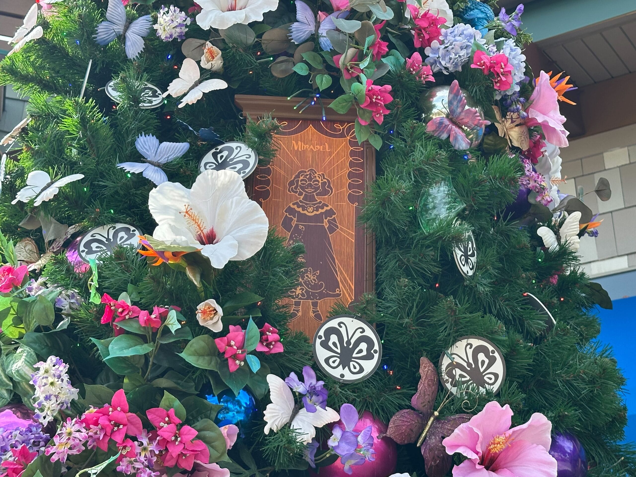 Floral wreath with colorful flowers, butterflies, and a wooden plaque featuring a carved design in the center.