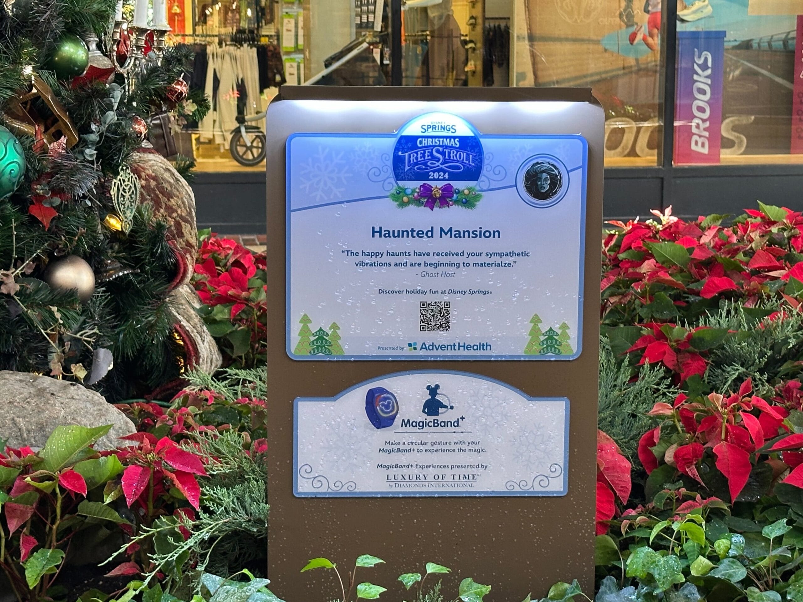 A Christmas tree display sign for Haunted Mansion, featuring sponsorship details and decorations with poinsettias and a Christmas tree.
