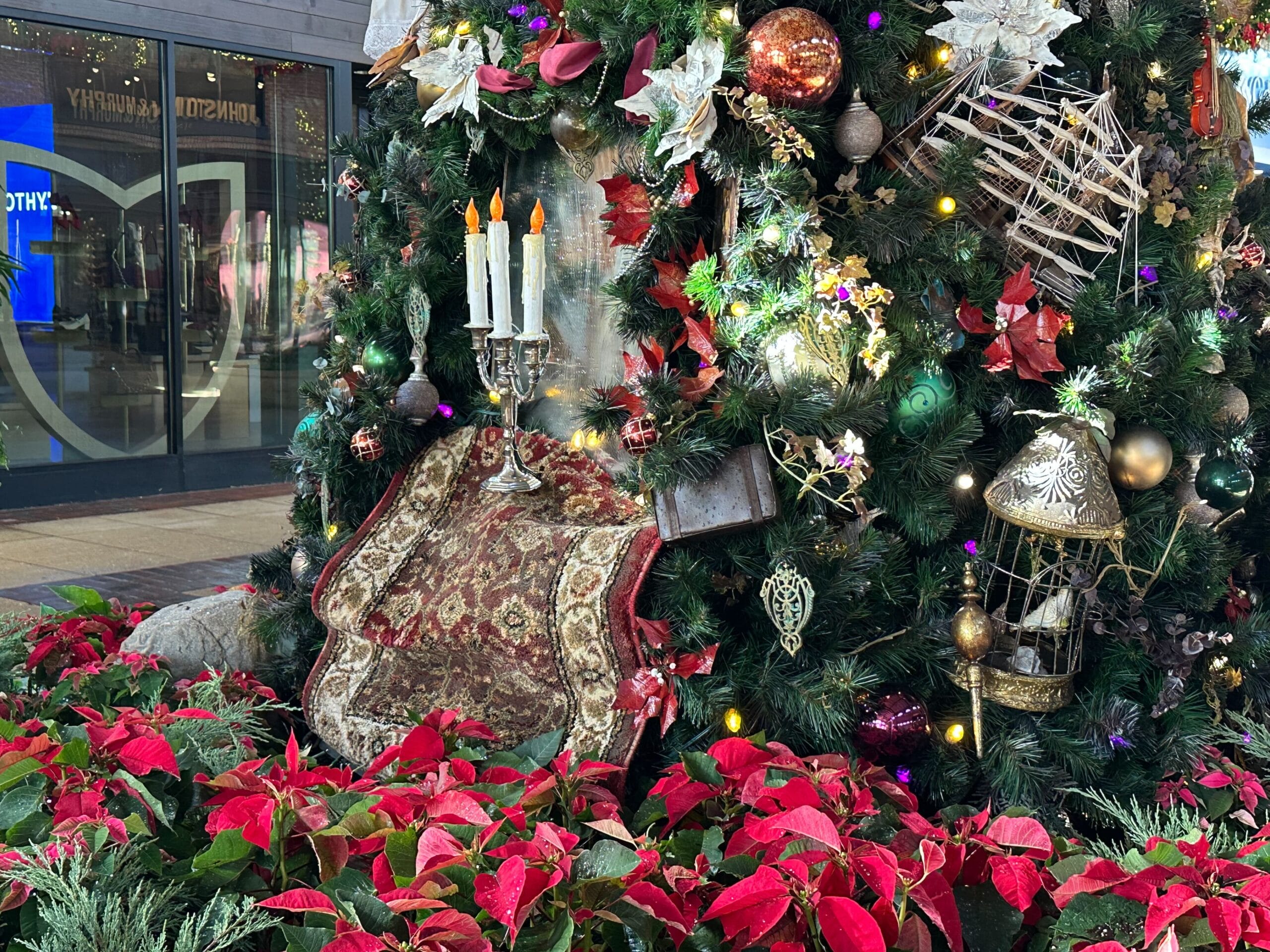 A decorated Christmas tree with red and white ornaments, candles, and a patterned chair nearby. Poinsettias are arranged at the base.