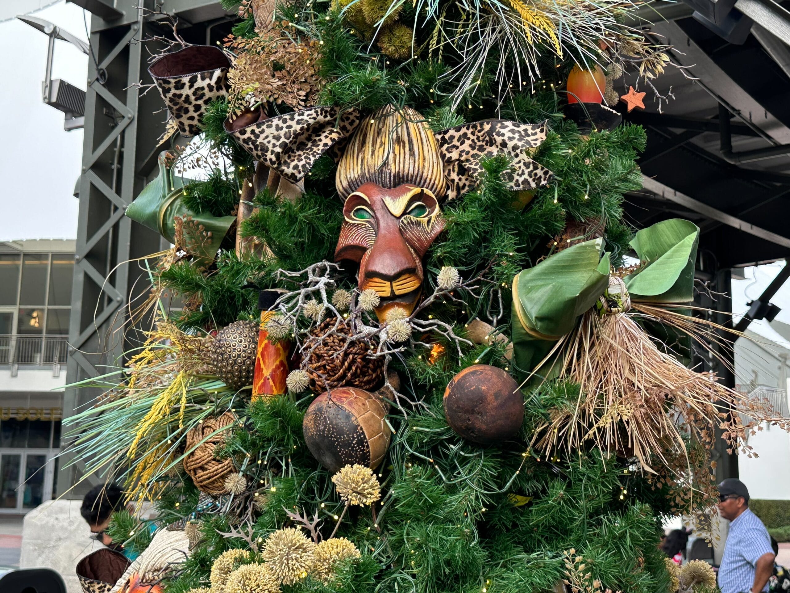 A decorative tree adorned with a lion-like mask, greenery, dried plants, and animal print fabric.