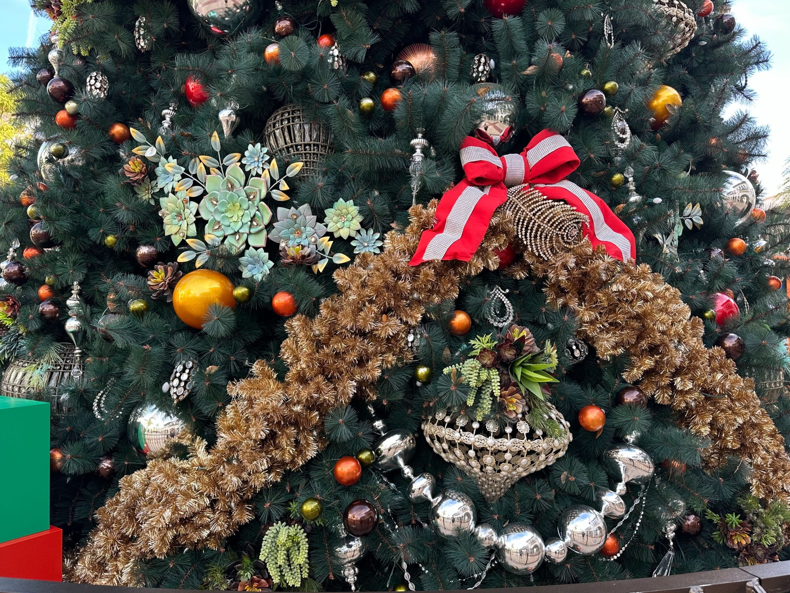 Decorated Christmas tree with ornaments, a large golden garland, and a red and white bow.