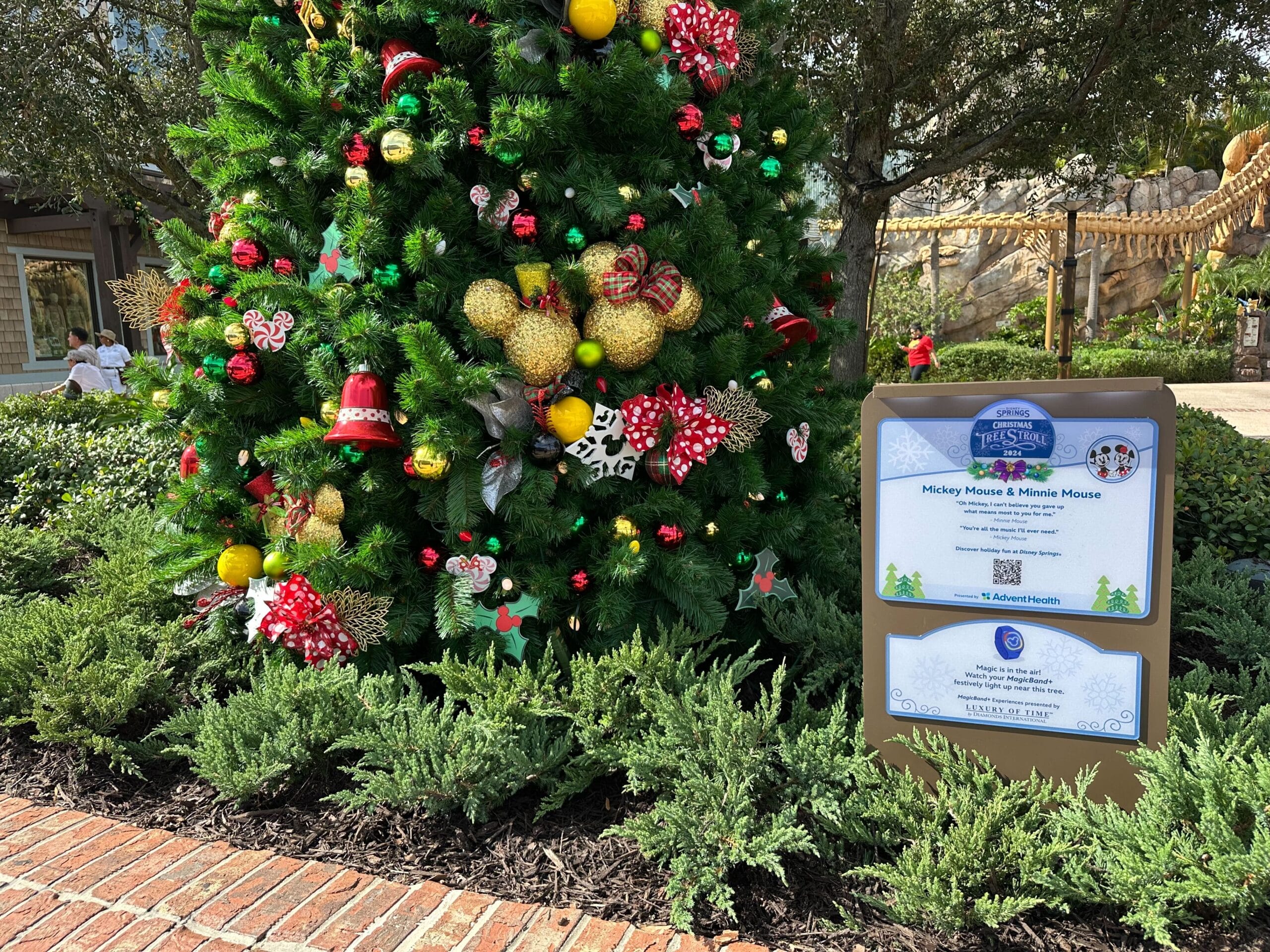 Decorated Christmas tree with red and gold ornaments beside a signage stand in a garden setting.