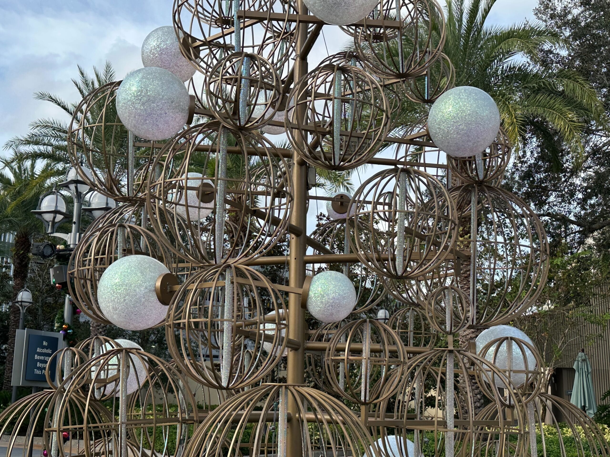 A metal sculpture with spherical frames and white globe lights set against a background of palm trees.