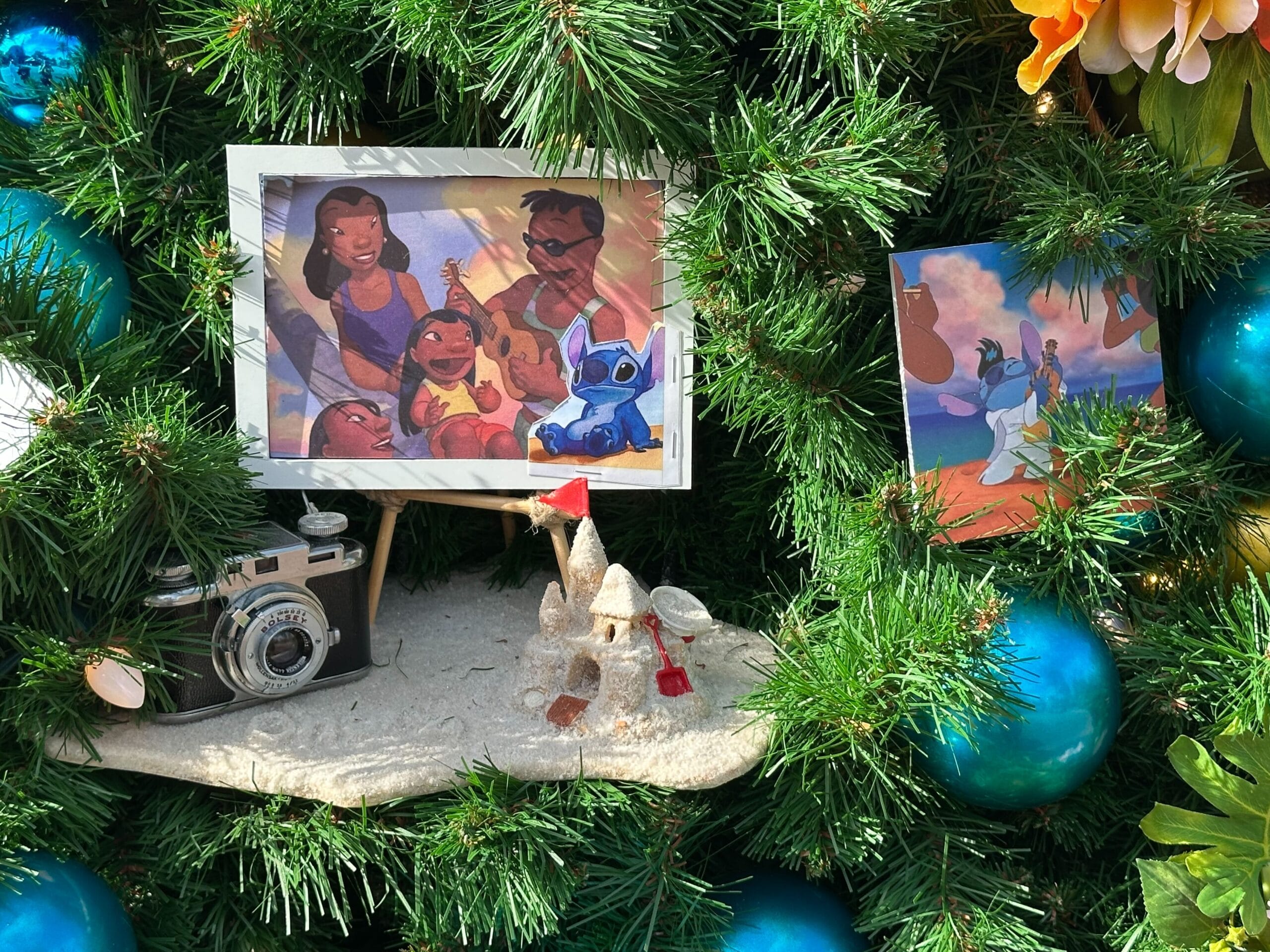 Photos of cartoon characters and a toy camera are displayed on a Christmas tree with blue ornaments and a sandcastle decoration.