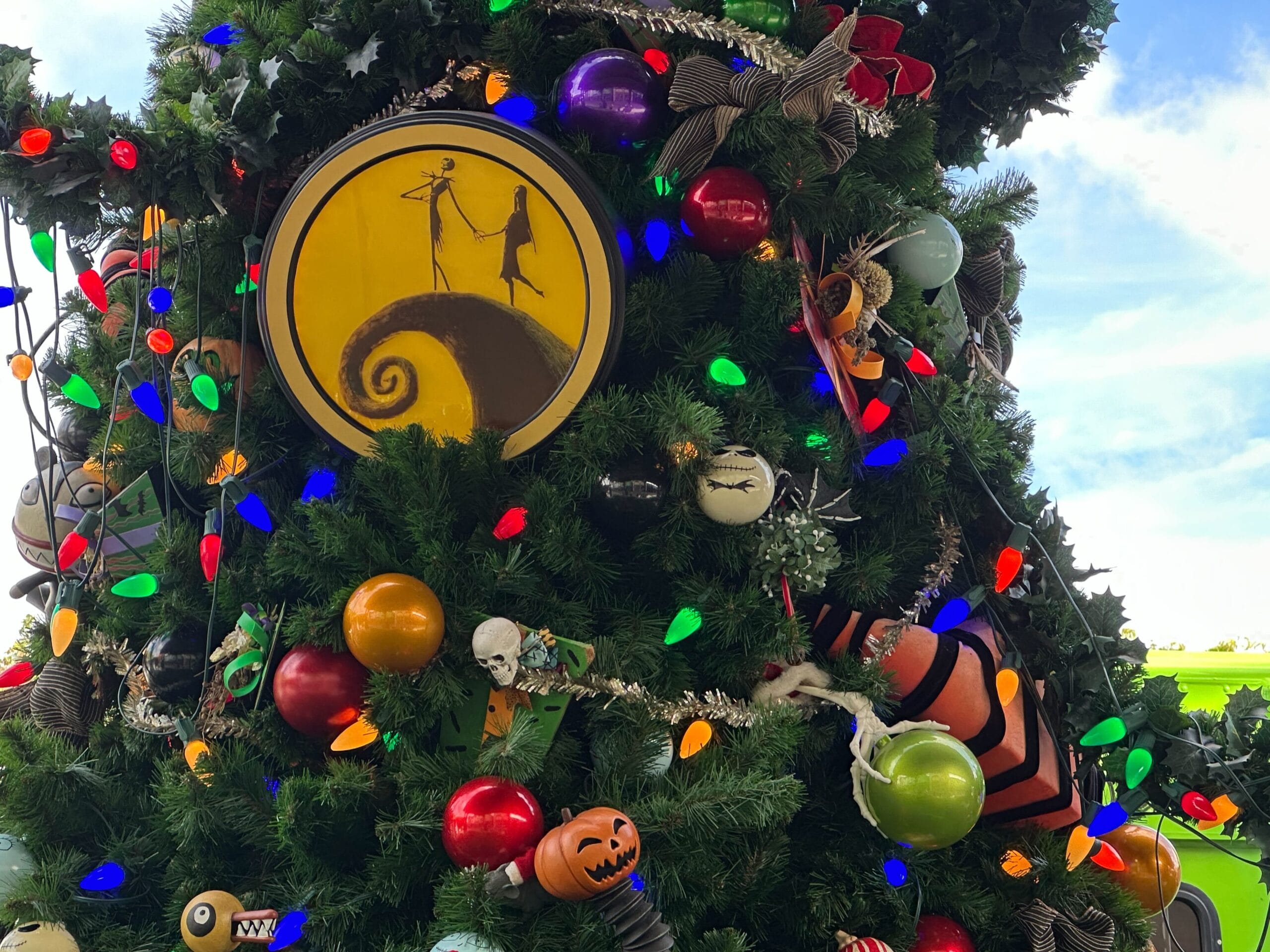 A Christmas tree decorated with colorful lights and ornaments, featuring a yellow circle with a black silhouette of two figures on a spiraled hilltop scene.