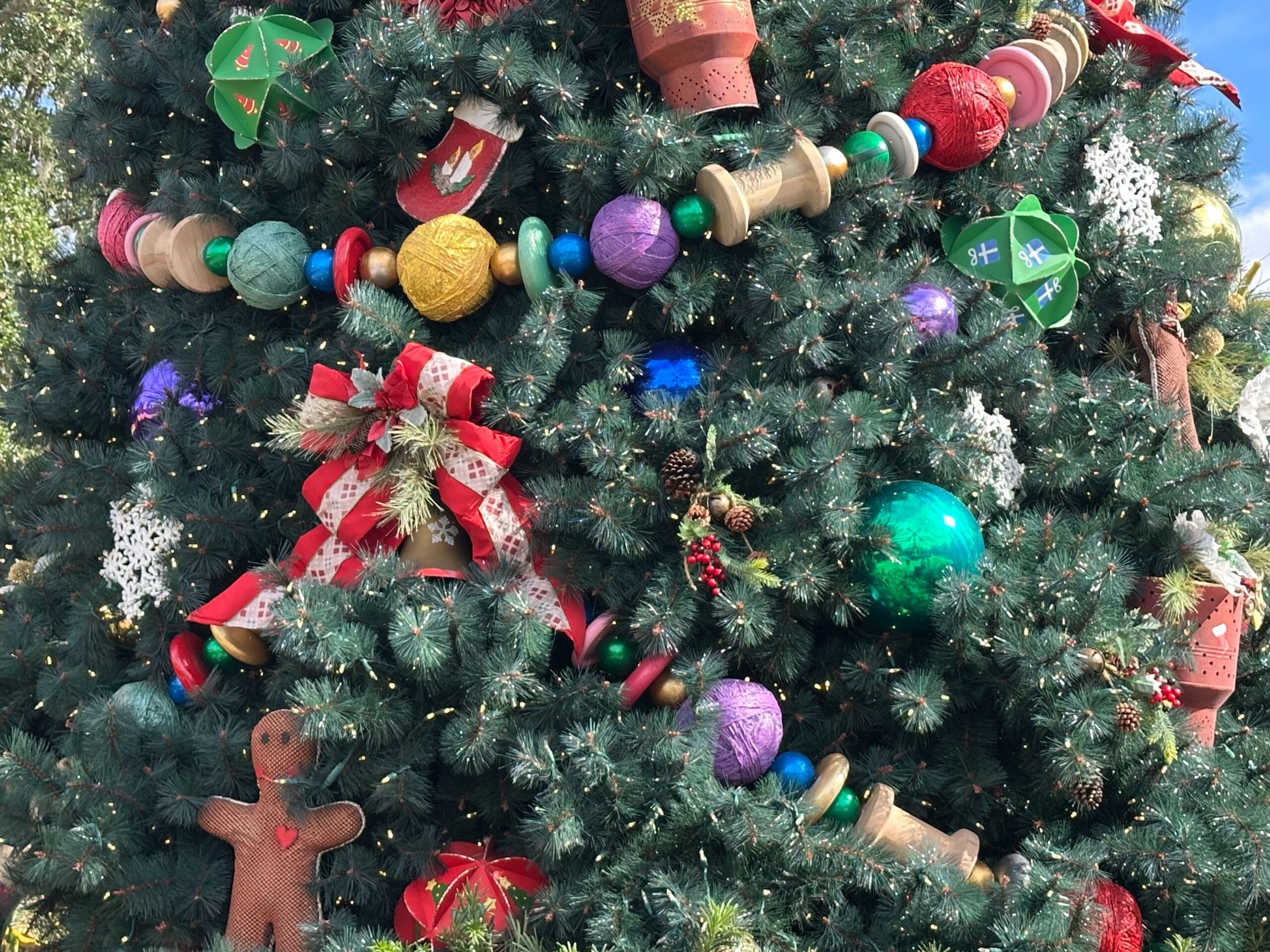A Christmas tree decorated with colorful ornaments, including large spools, balls, a gingerbread figure, and festive bows.