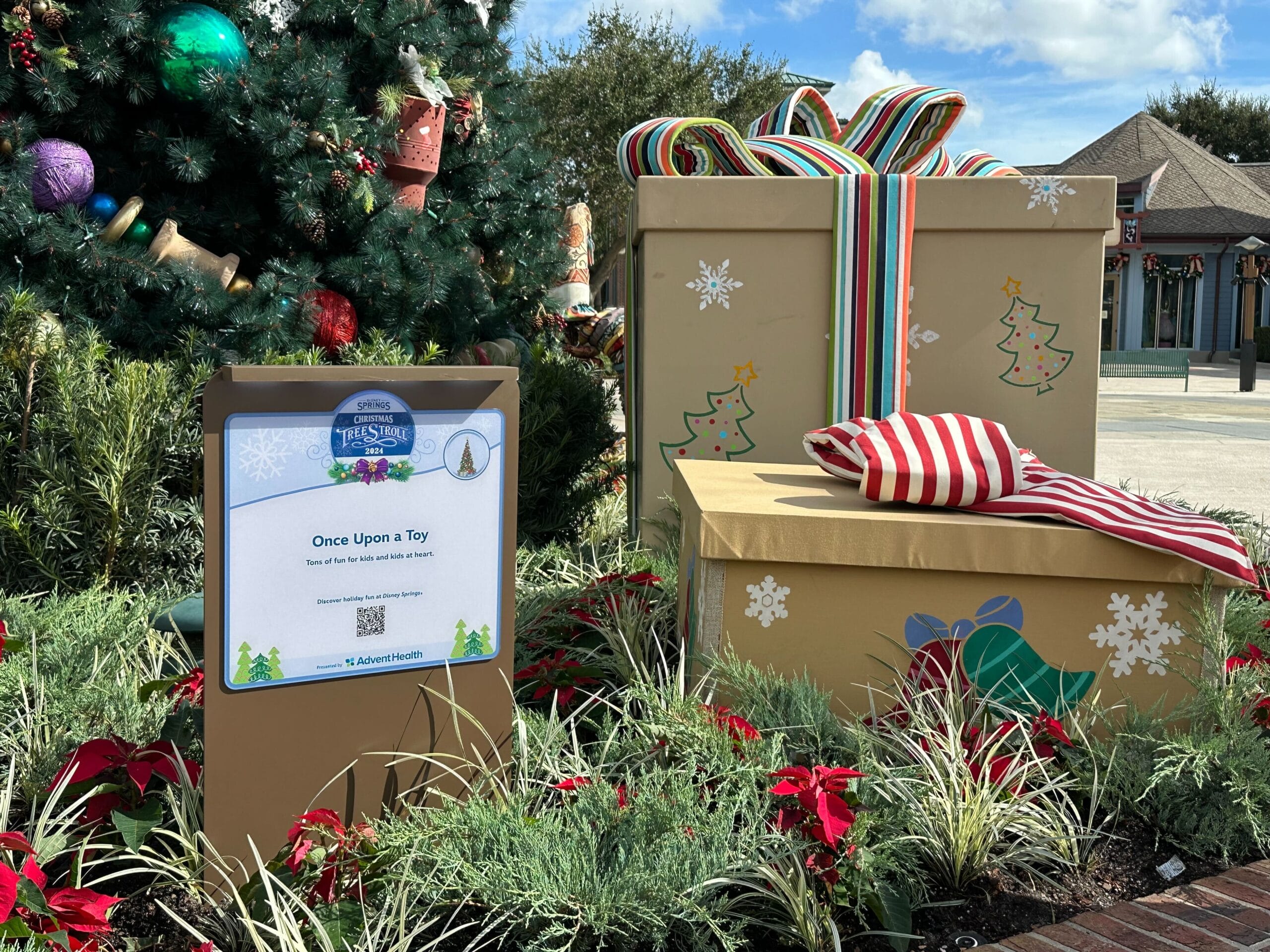 Holiday display with decorated Christmas tree and large gift boxes. Sign reads "Once Upon a Toy" with festive decorations and QR code.
