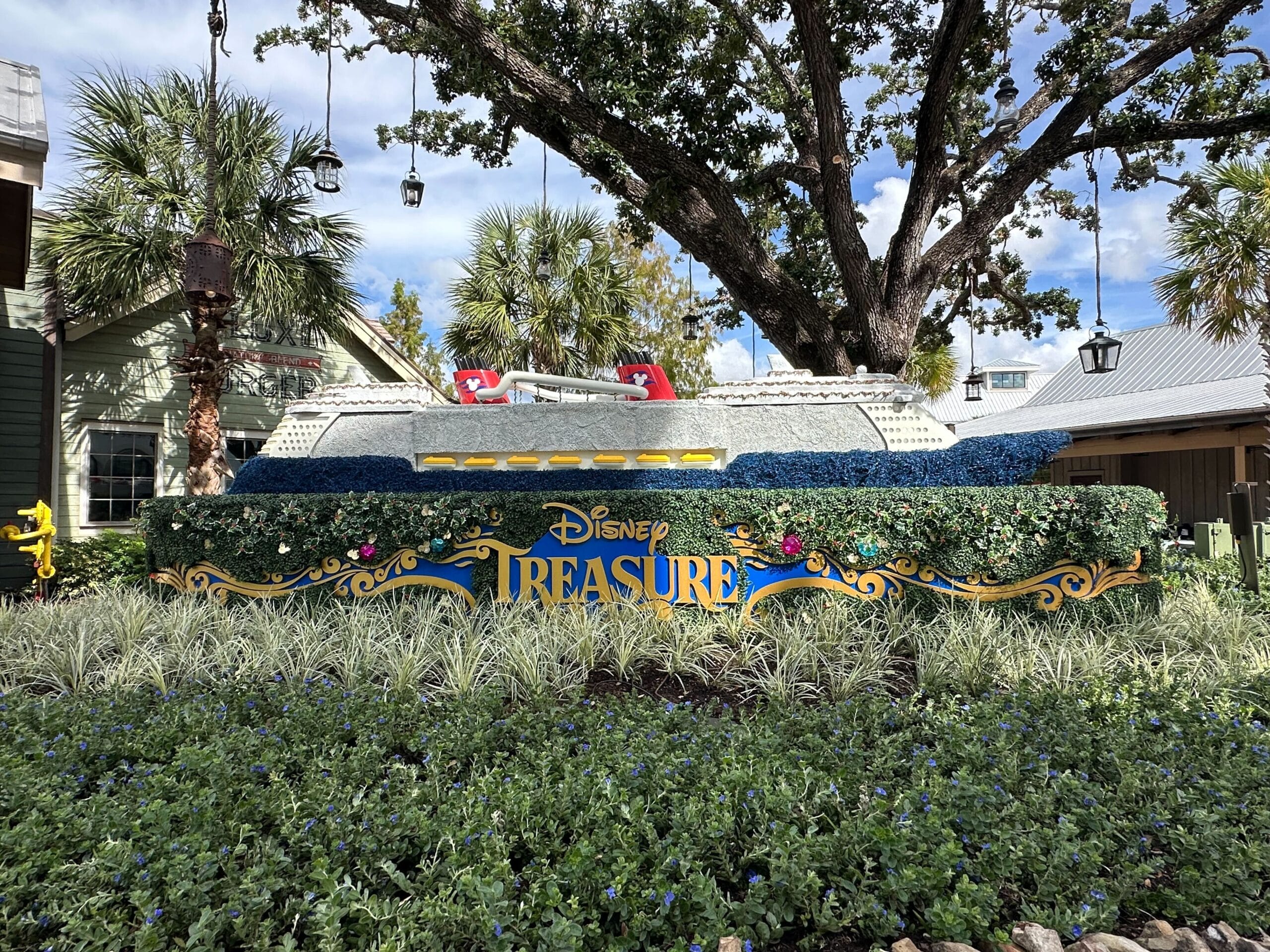 A decorative display with a model ship and "Disney Treasure" sign surrounded by greenery and flowers.