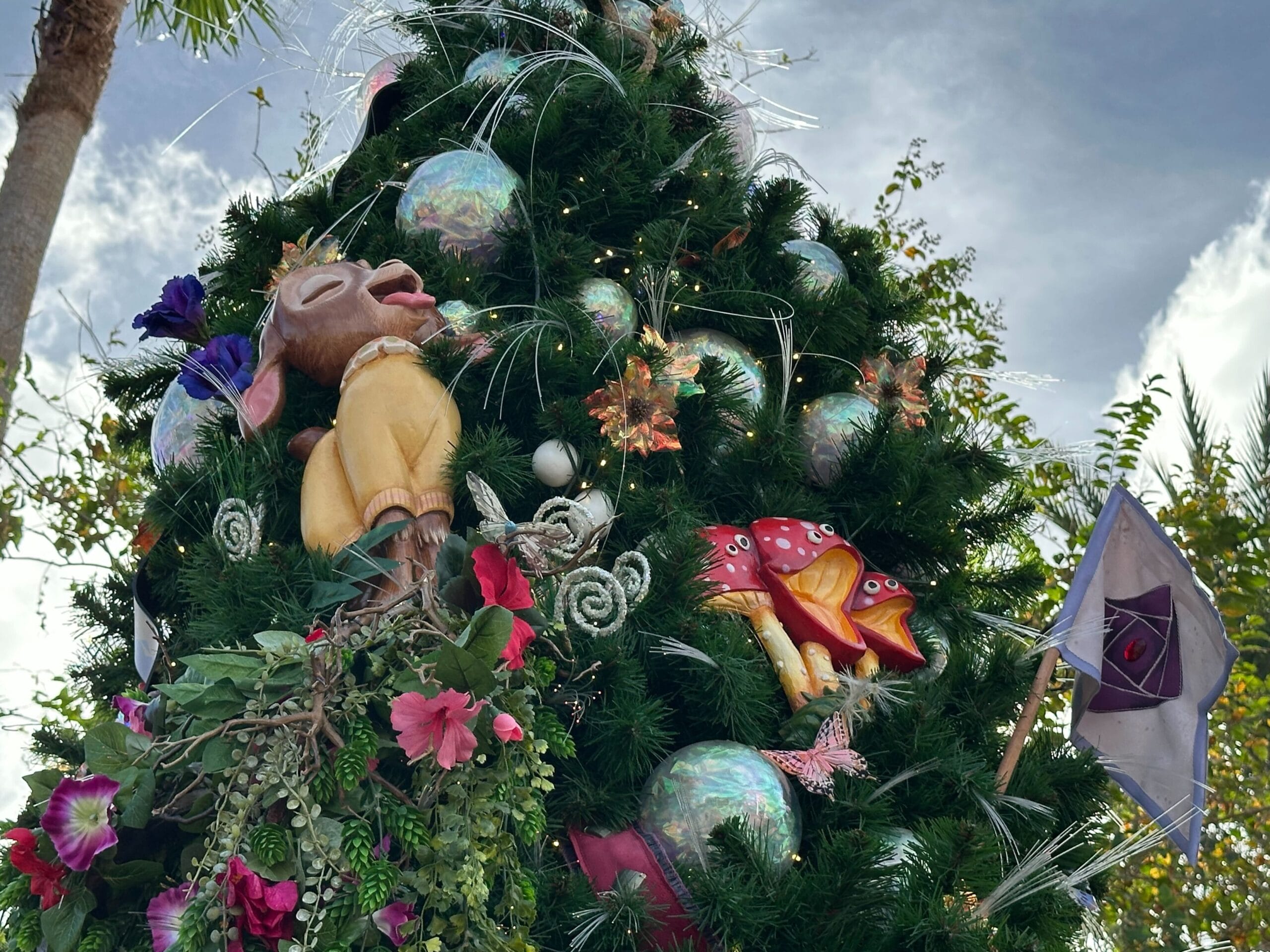 A decorated Christmas tree with colorful ornaments, flowers, and a character figure. The background shows a clear sky and palm trees.