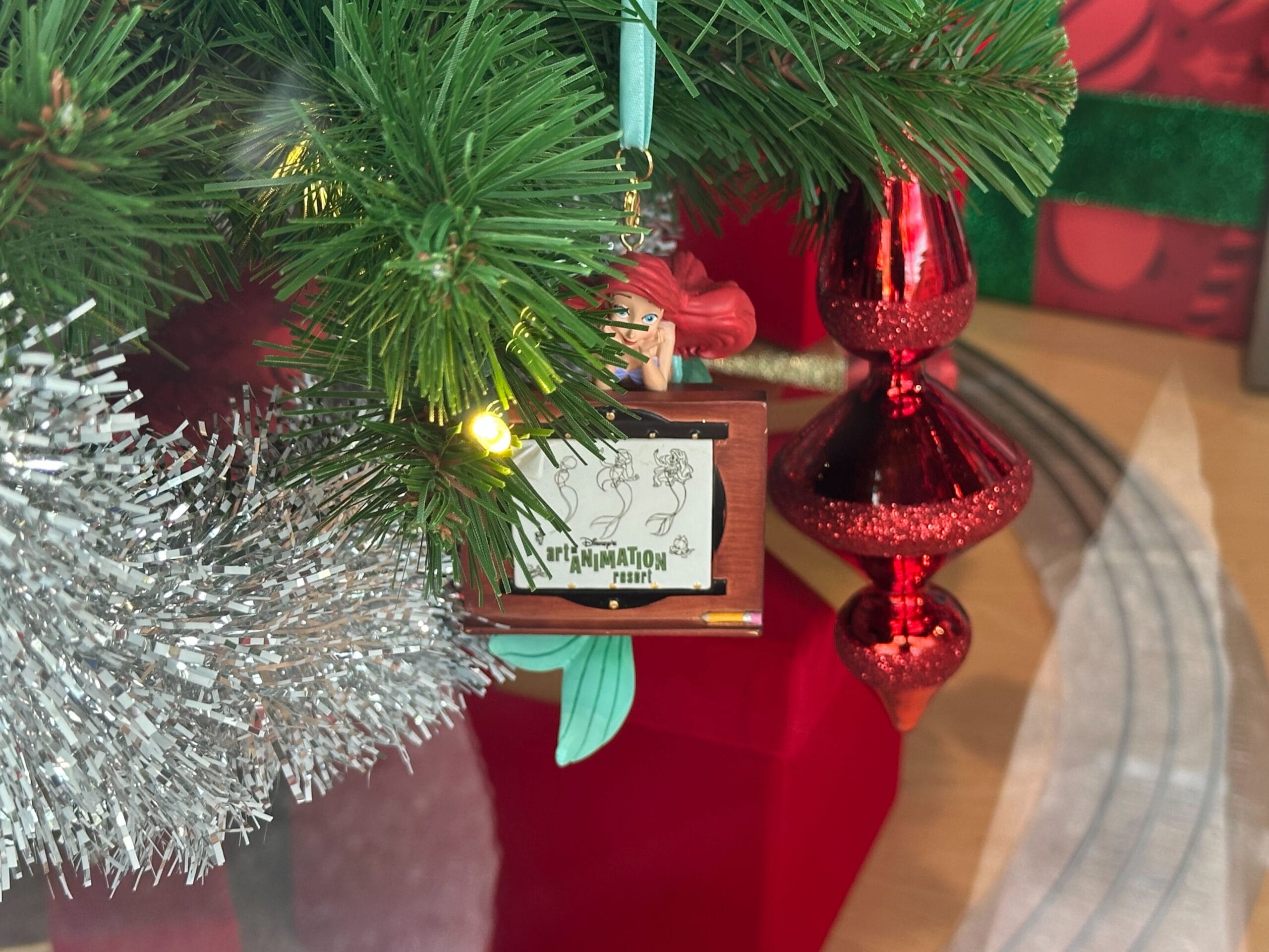 A decorated Christmas tree with a glittering silver garland and a red ornament. A small screen ornament displays "Animation" with sketches of characters.