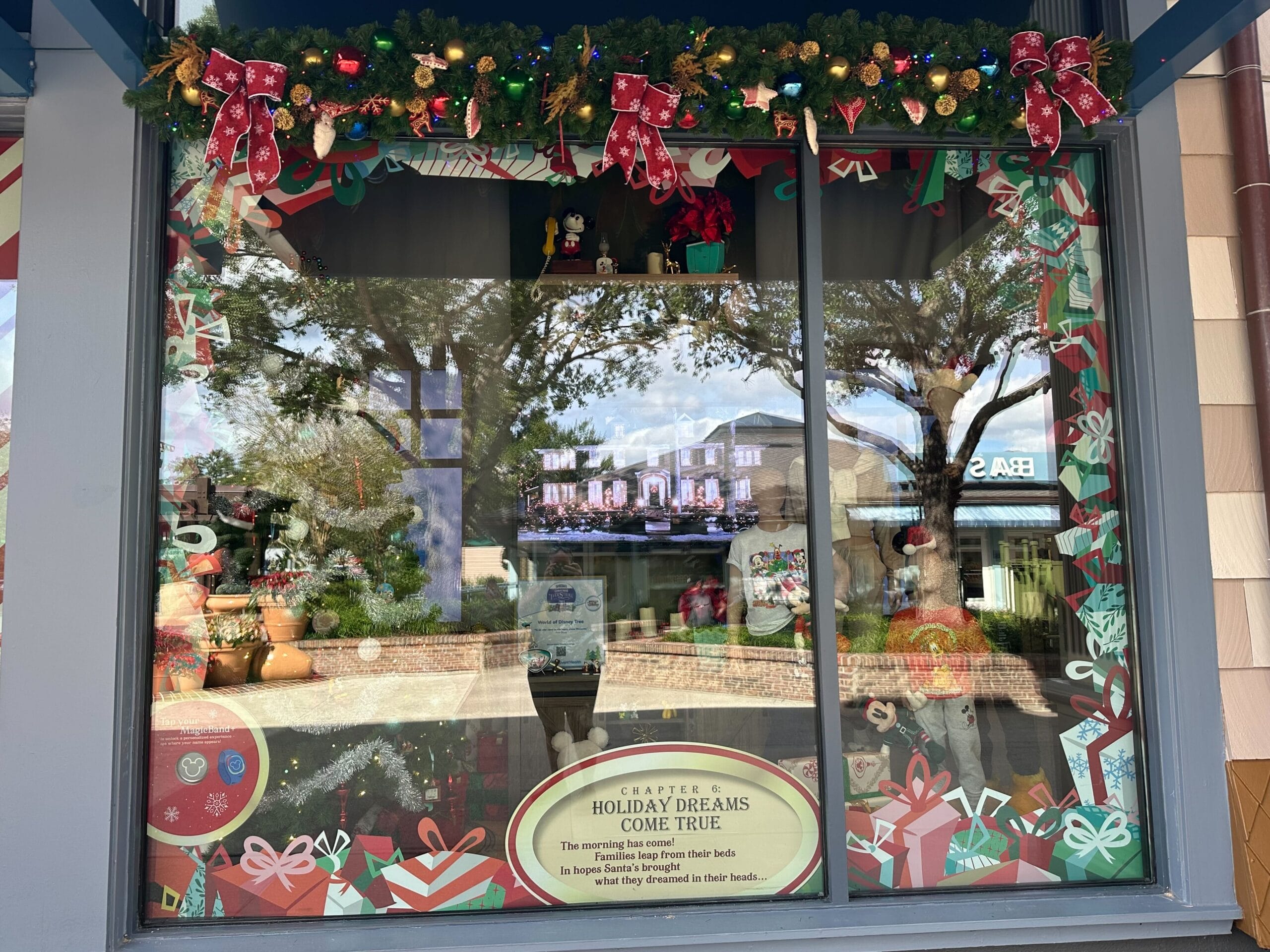 A store window display with Christmas decorations, including gifts, ribbons, and ornaments. There's a sign saying "Holiday Dreams Come True" and a small digital screen showing a house.