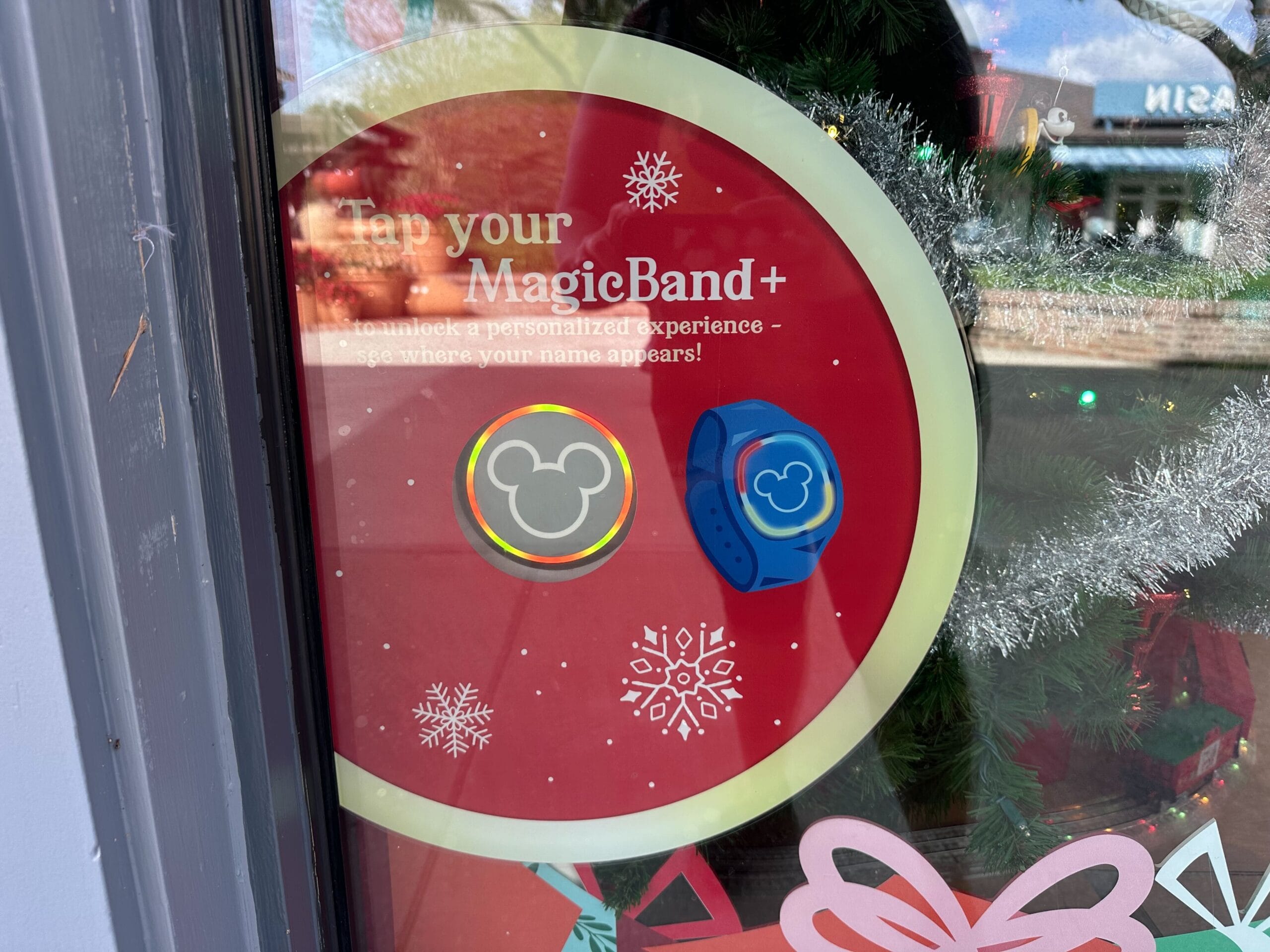 Display of MagicBand+ in a store window, featuring two wristbands with Mickey Mouse symbols on a red backdrop with snowflake designs.