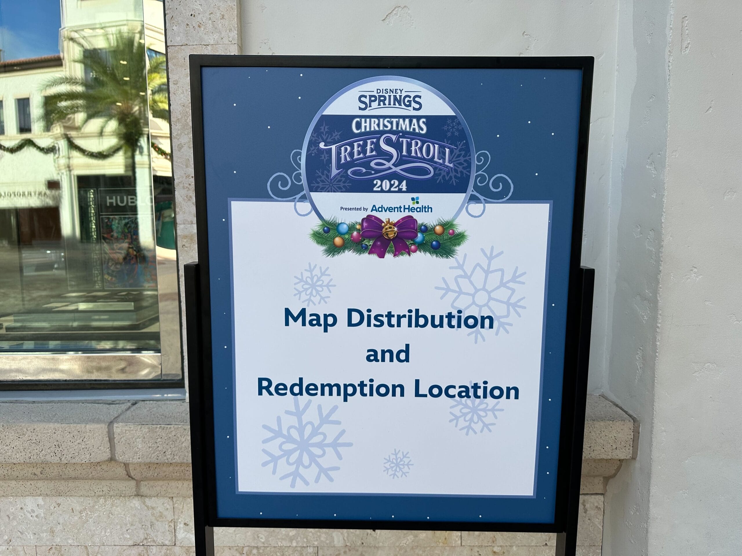 Sign for Disney Springs Christmas Tree Stroll 2024, decorated with festive snowflakes, indicating the "Map Distribution and Redemption Location.