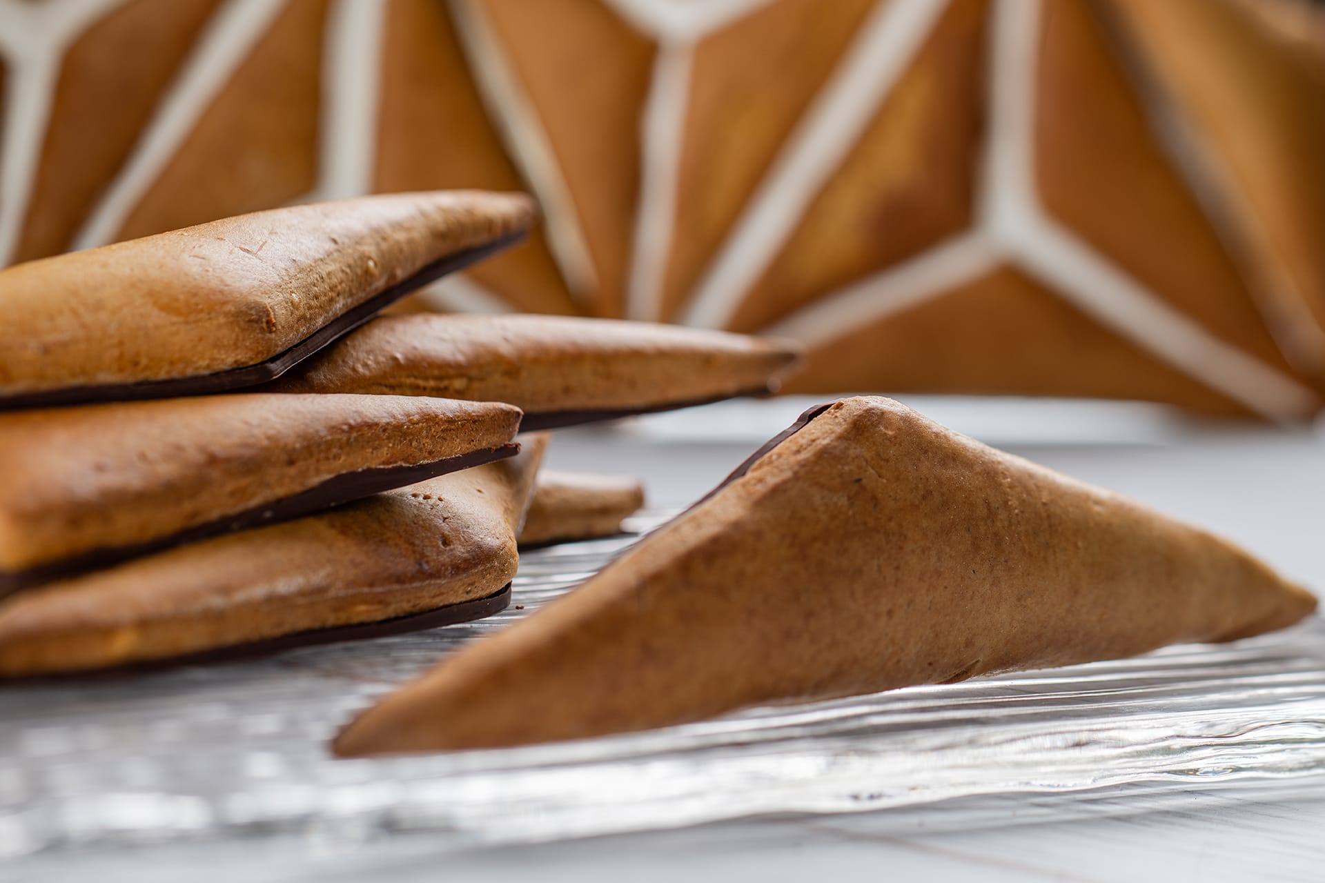 A close-up of triangular gingerbread cookies stacked on a table, perfectly complementing the geometric patterned background, captures the festive spirit of the holidays.