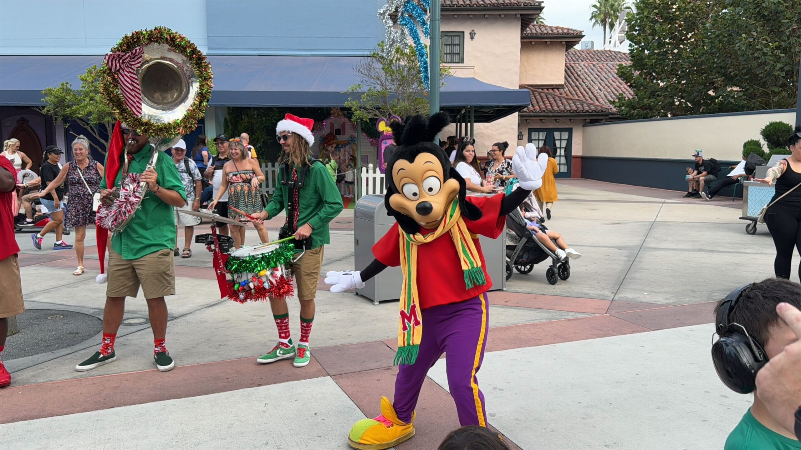 A character in a colorful outfit poses for a photo while a band plays festive music in the background.