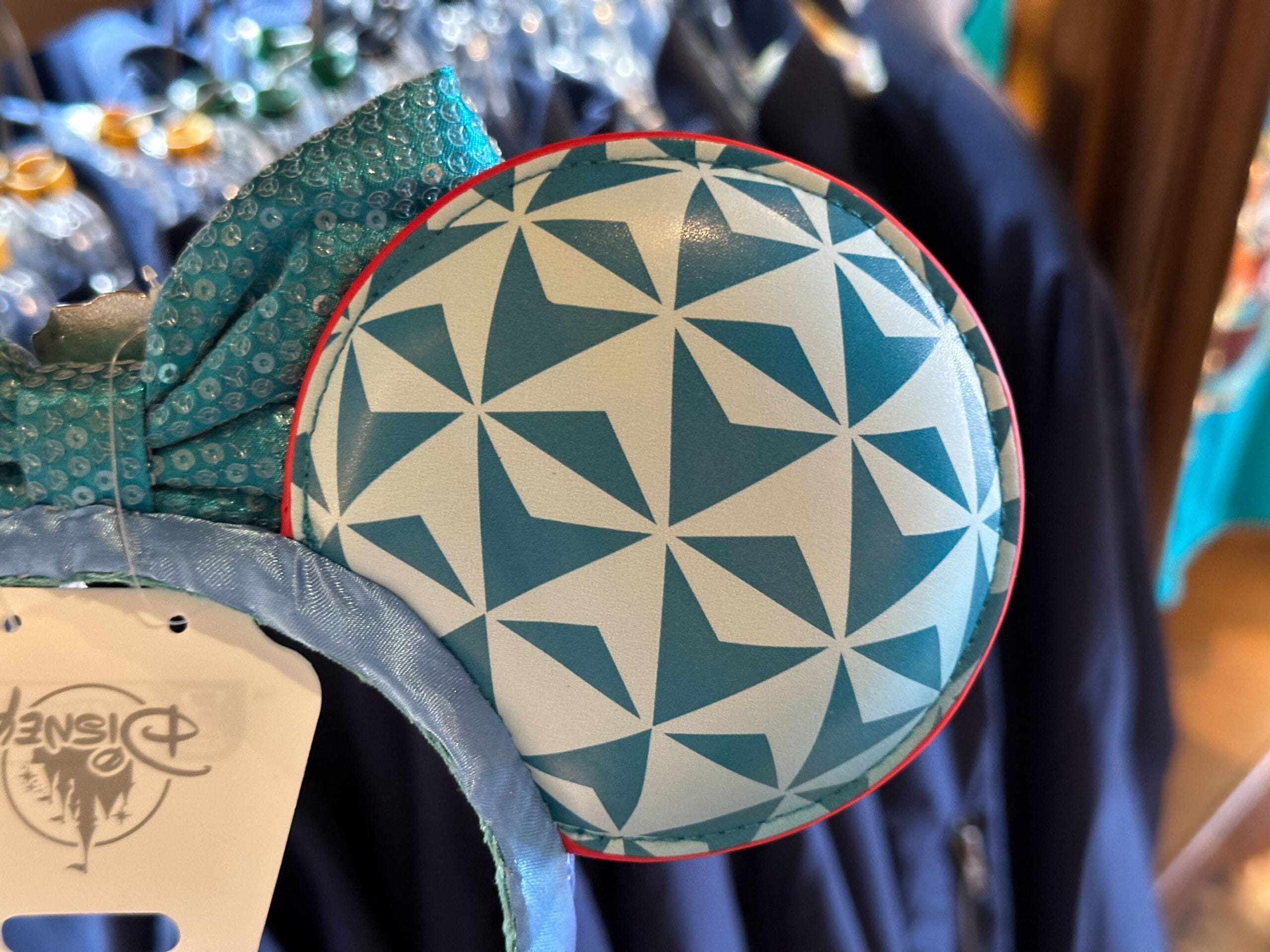 Close-up of a blue and white patterned circular ear on a headband with a blue bow. Disney tag visible in the background.