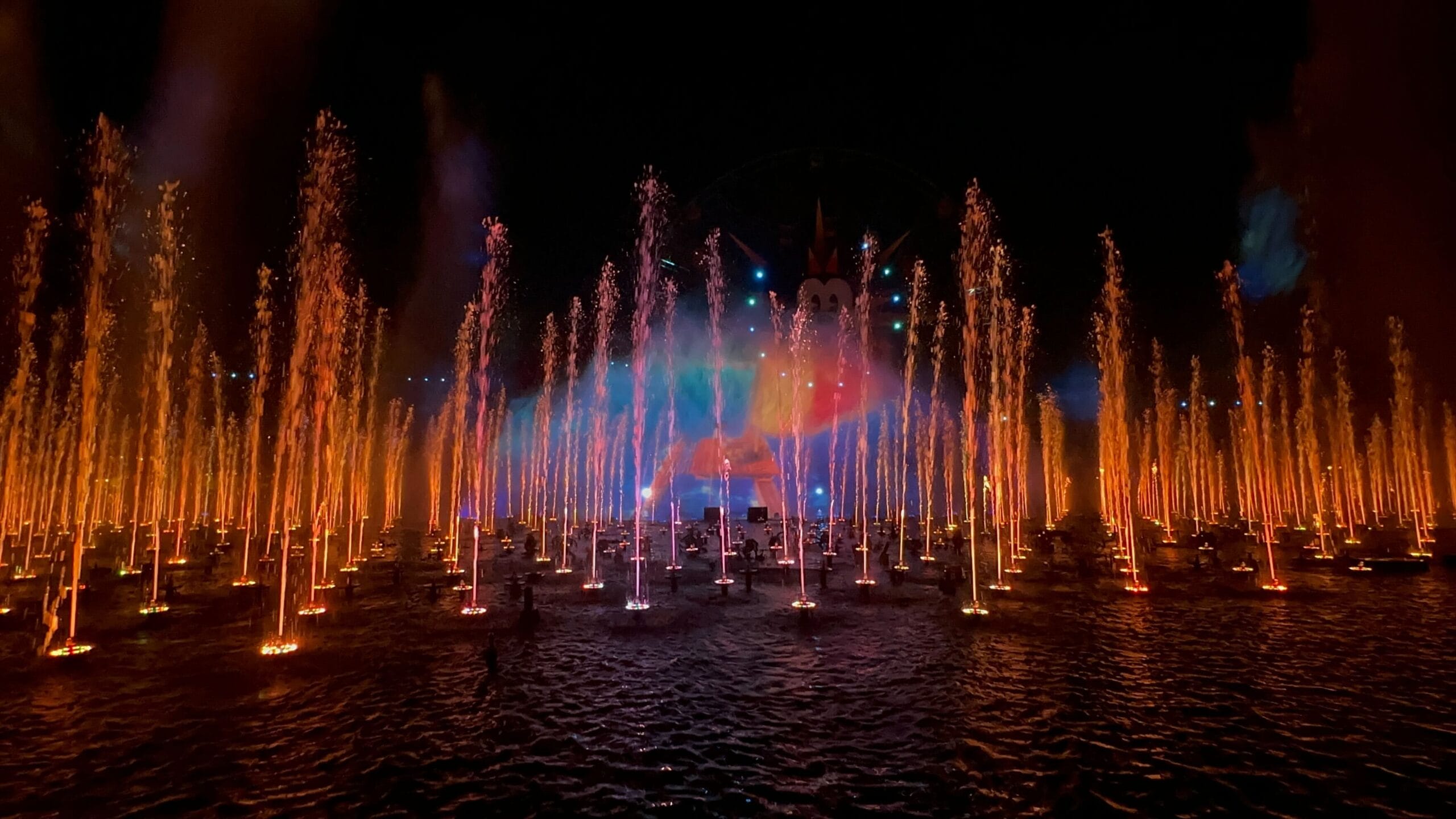 The World of Color nighttime water show at Disney California Adventure dazzles with illuminated fountains and colorful projections on water, set against a dark sky.