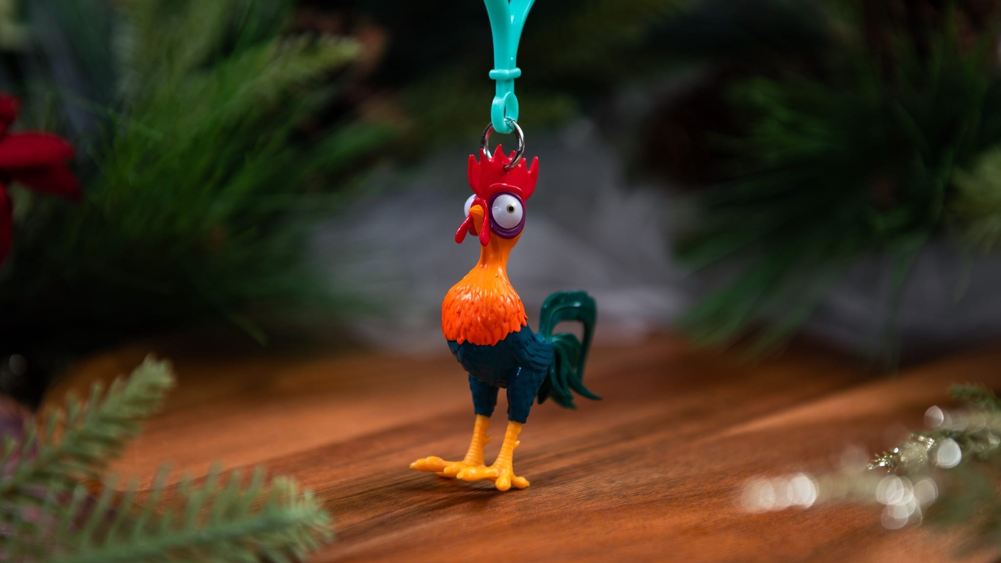 A colorful rooster keychain hangs in front of a blurred background with greenery.