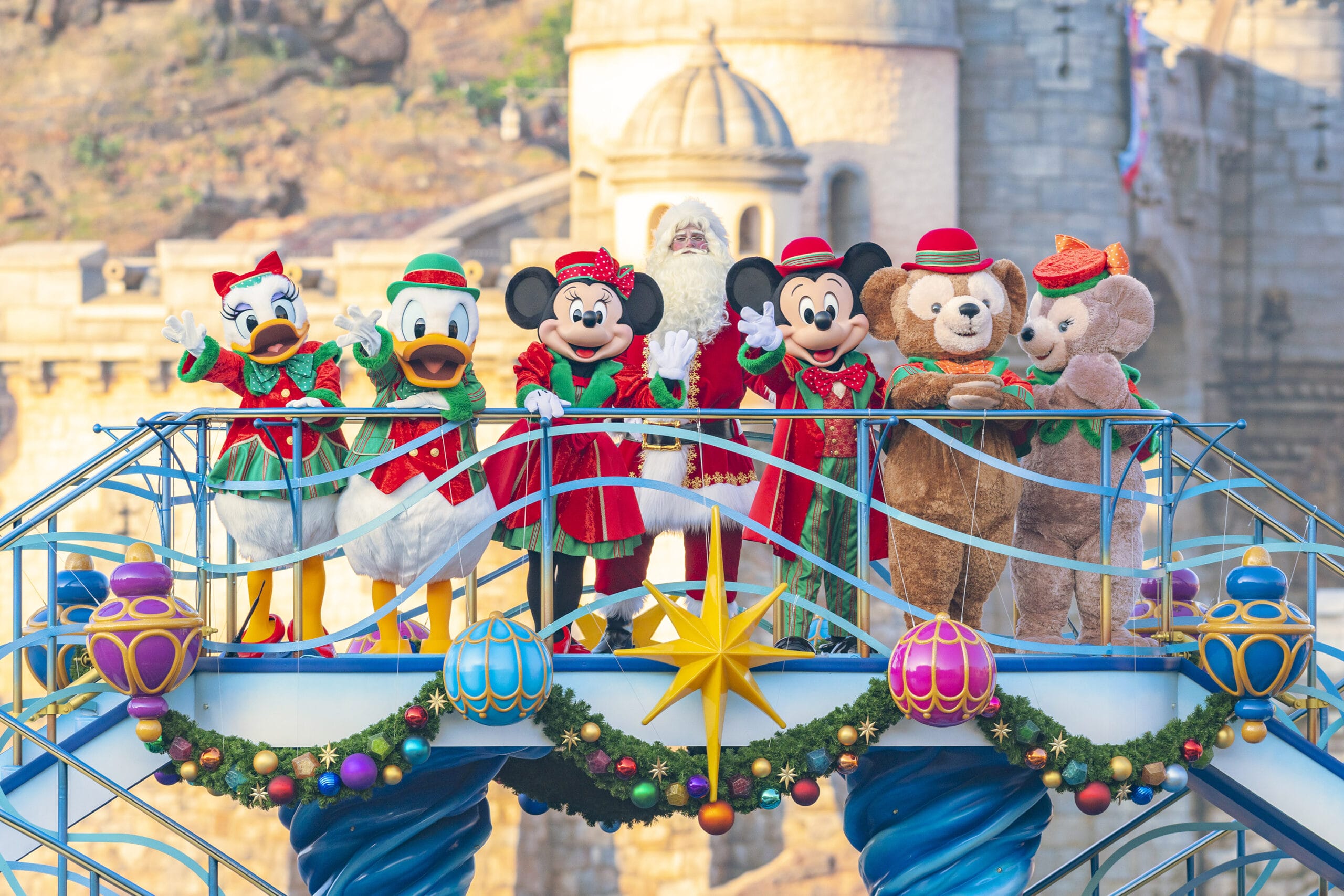 Characters in festive outfits stand on a decorated bridge with a castle in the background.