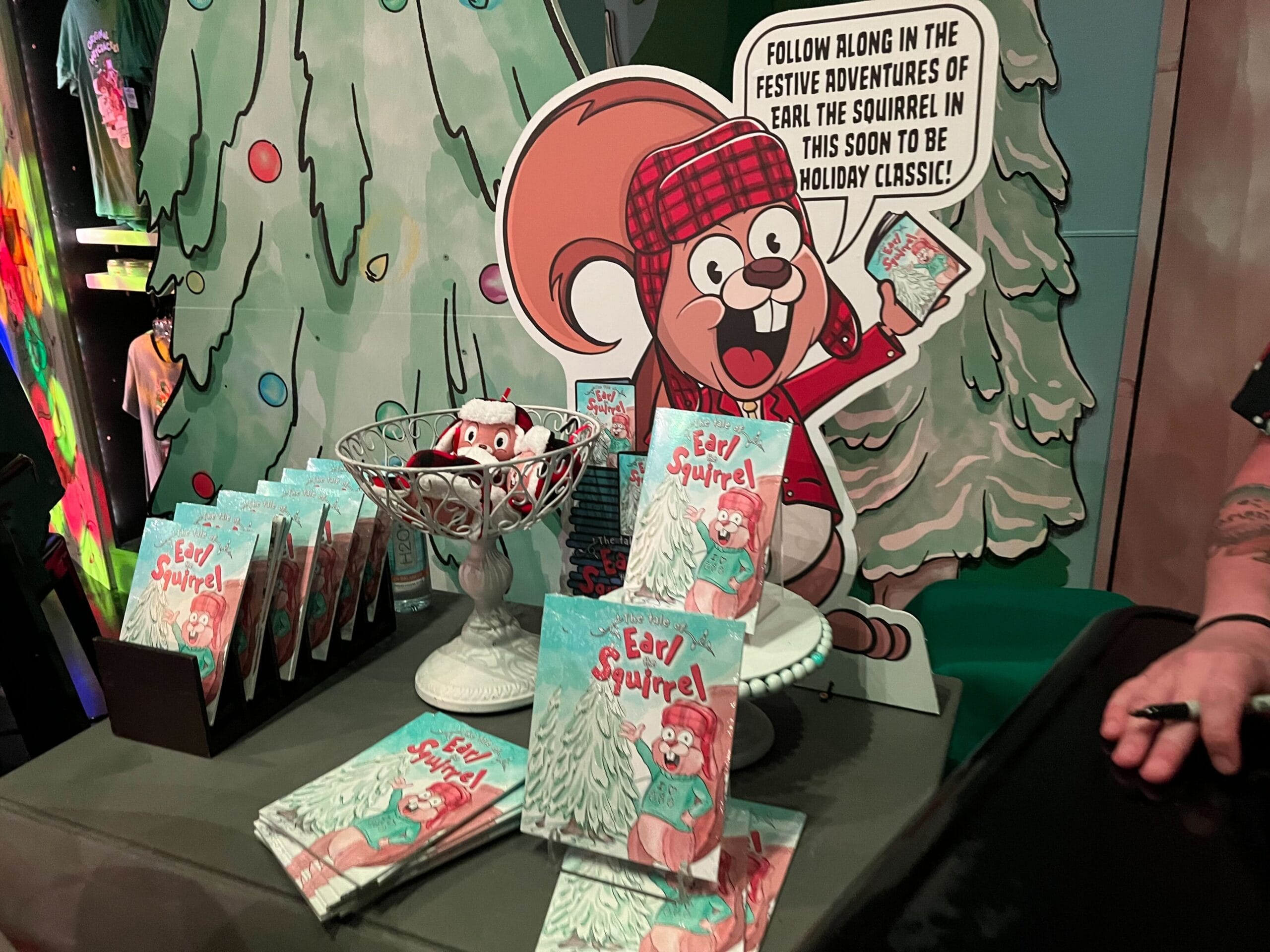 Display of "Earl the Squirrel" books with a large cutout of a cartoon squirrel wearing a plaid hat. Books are arranged on a table with holiday-themed decorations.