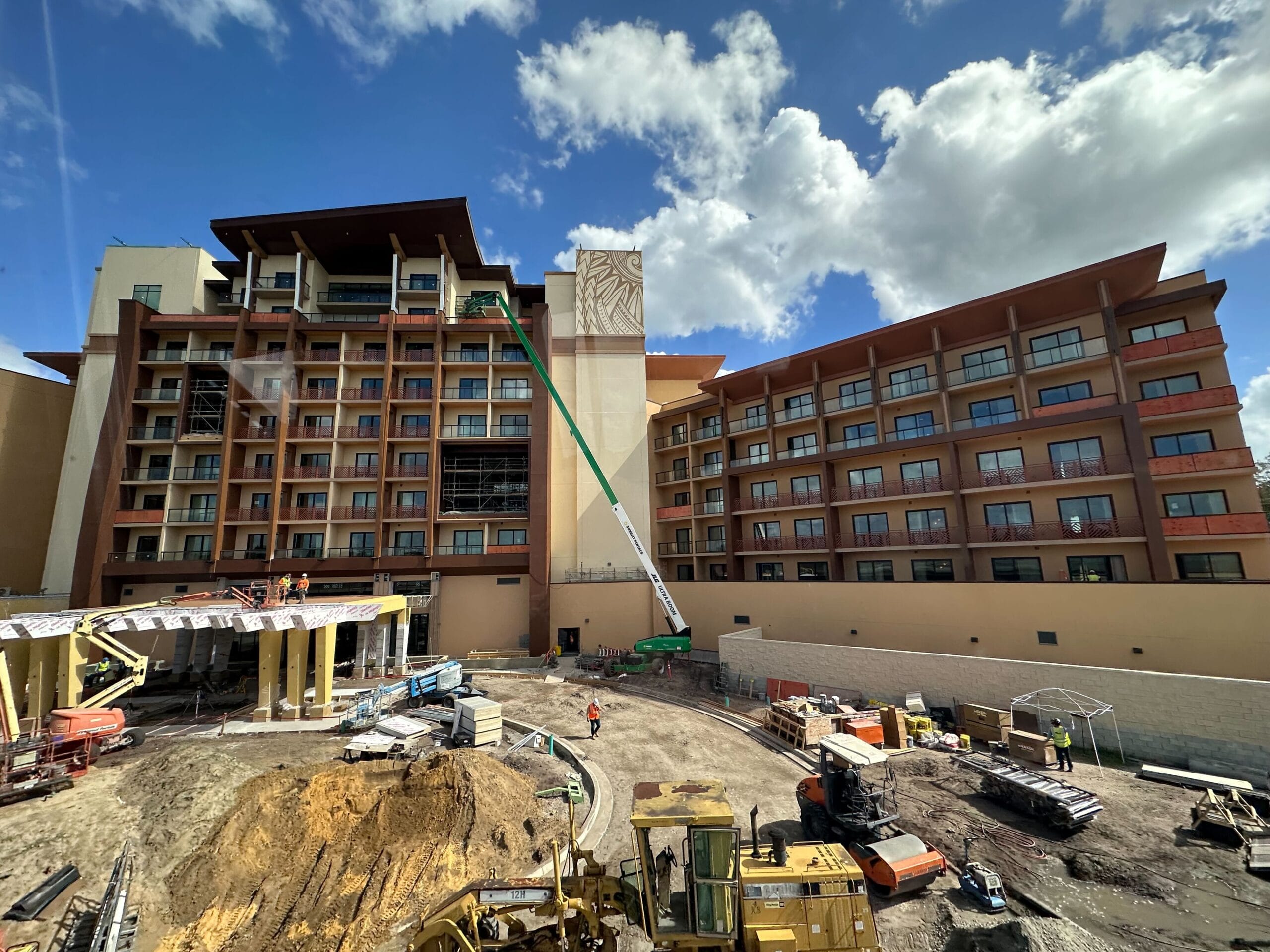 A bustling construction site unfolds in front of a multi-story building, where diligent workers and humming machinery converge. A green crane, almost reminiscent of an auto-draft sketch, is extended to the upper floors under a partly cloudy sky.
