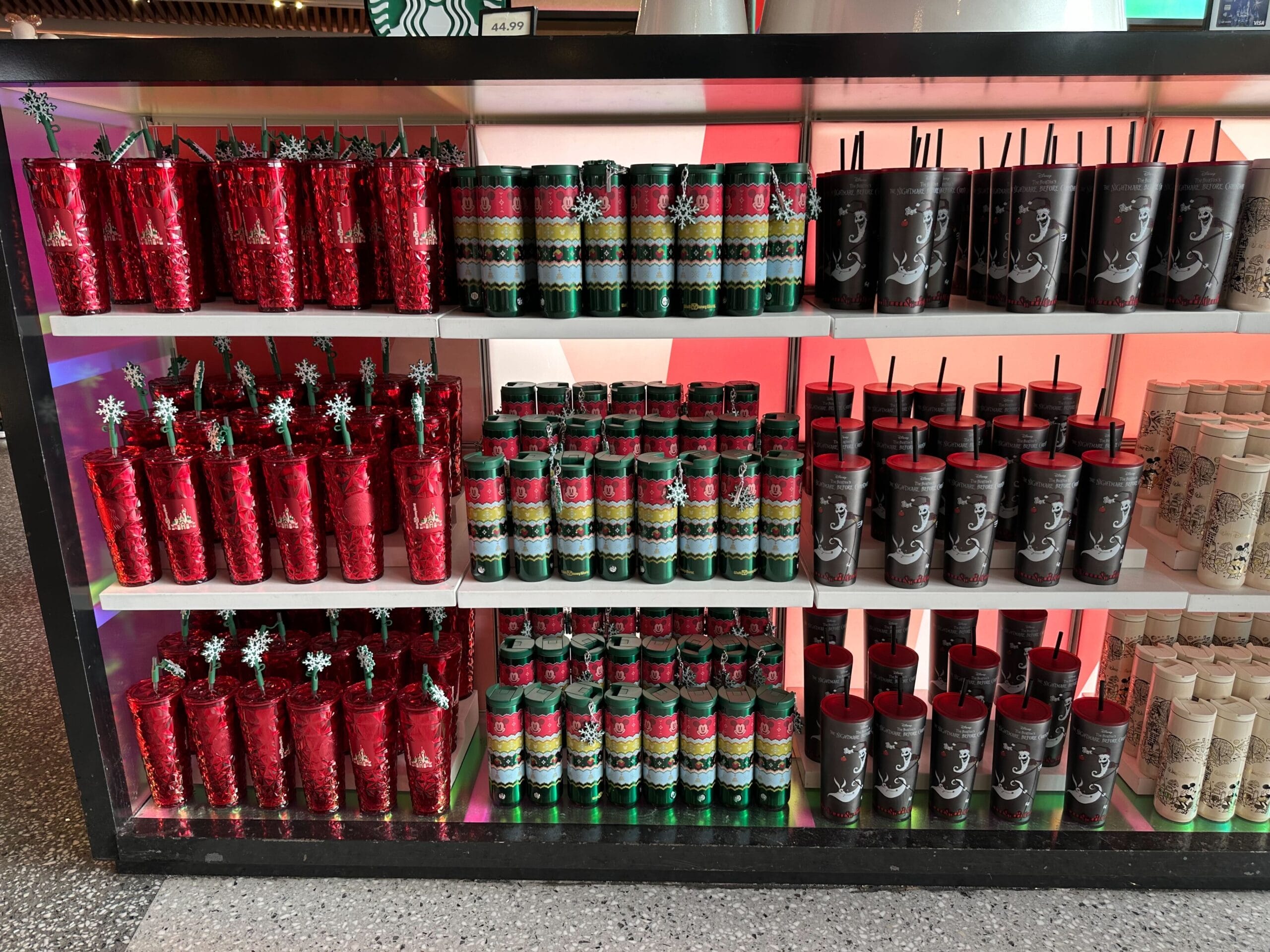 Shelves displaying a variety of colorful travel mugs and tumblers with festive designs in a store setting.