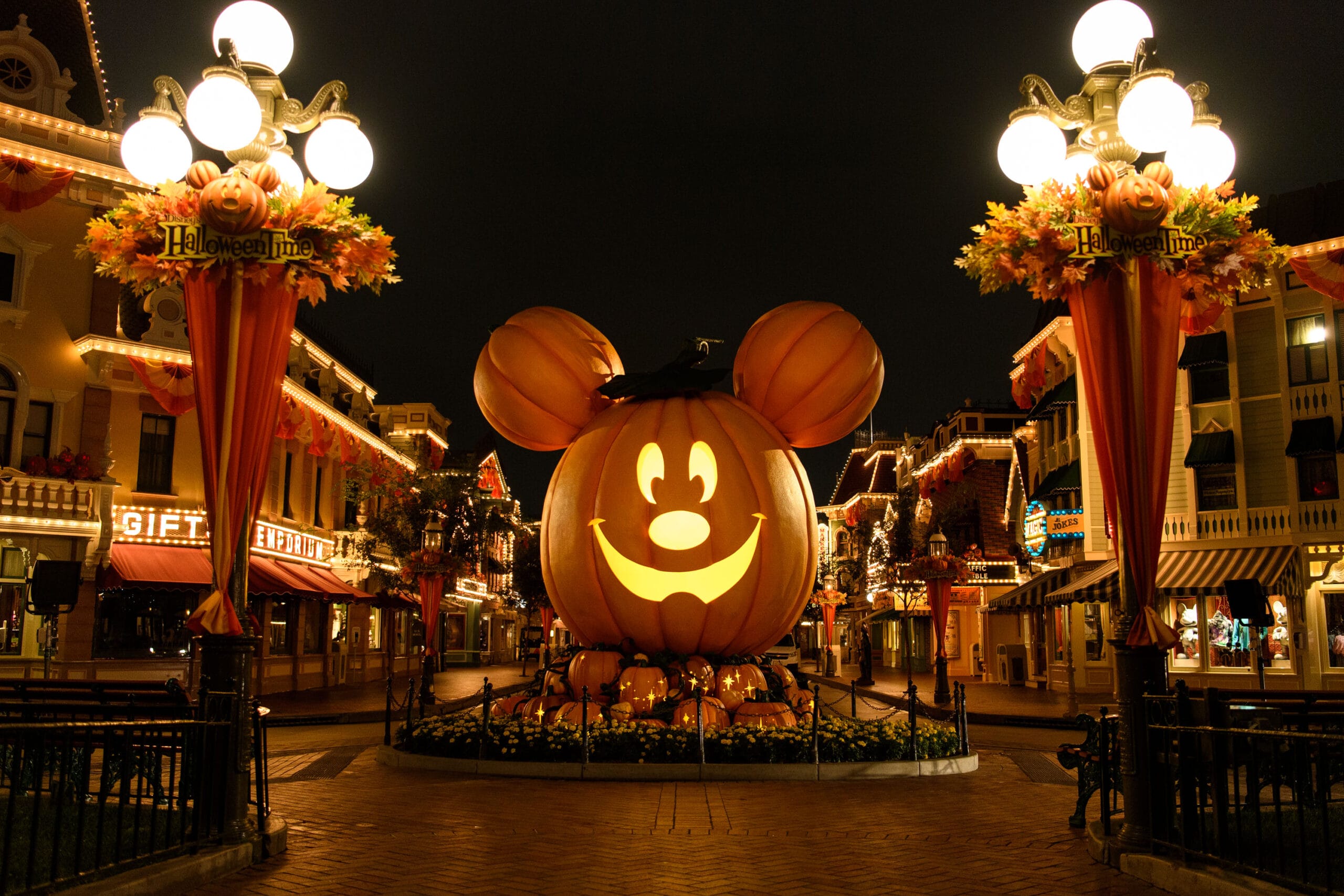 At Disneyland, a giant pumpkin grinning like Mickey Mouse lights up the night, surrounded by enchanting Halloween decorations. The magical display is set to captivate visitors throughout the 2025 event dates.