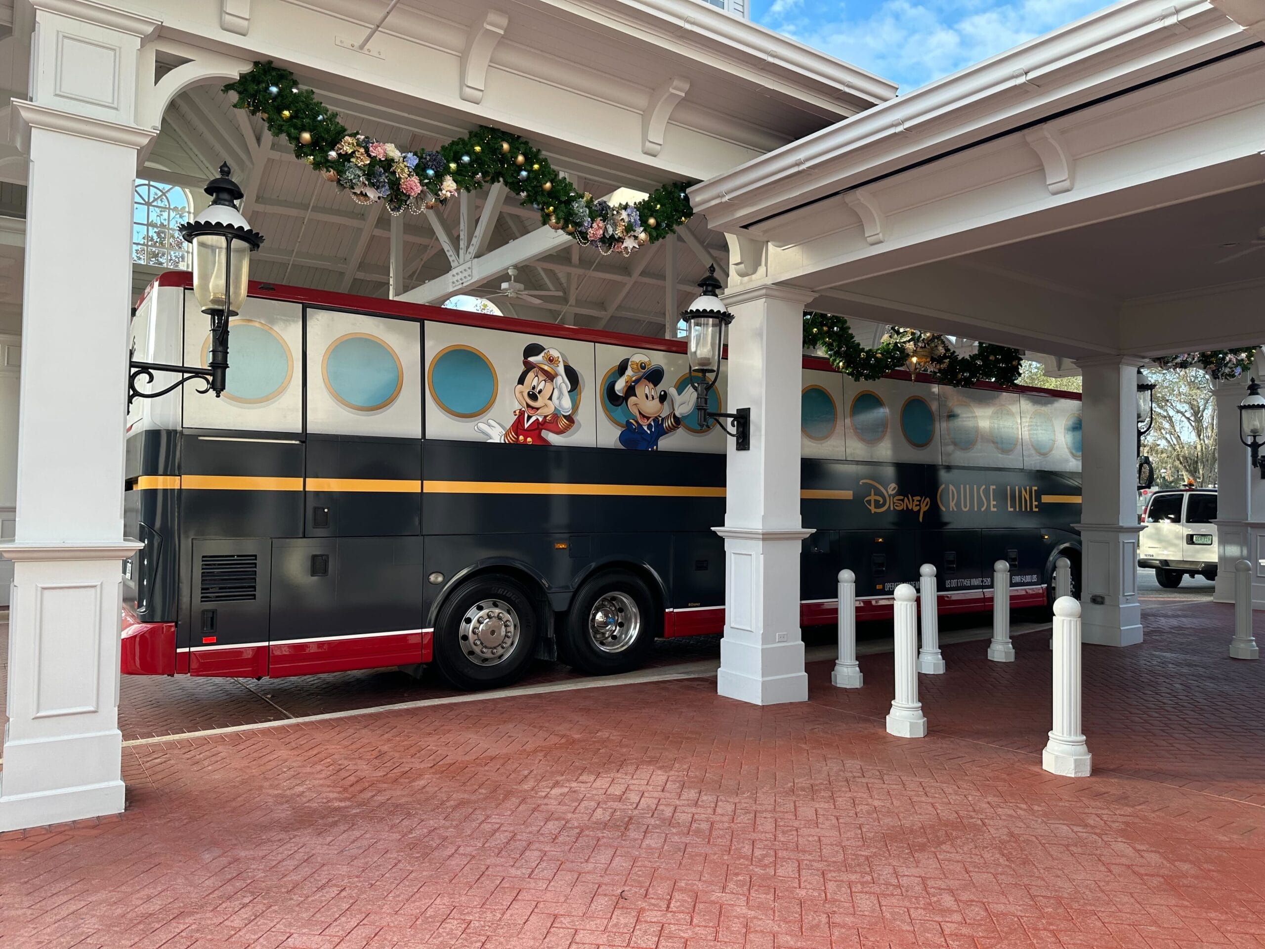 A Disney Cruise Line bus decorated with characters is parked under a canopy with floral garlands.