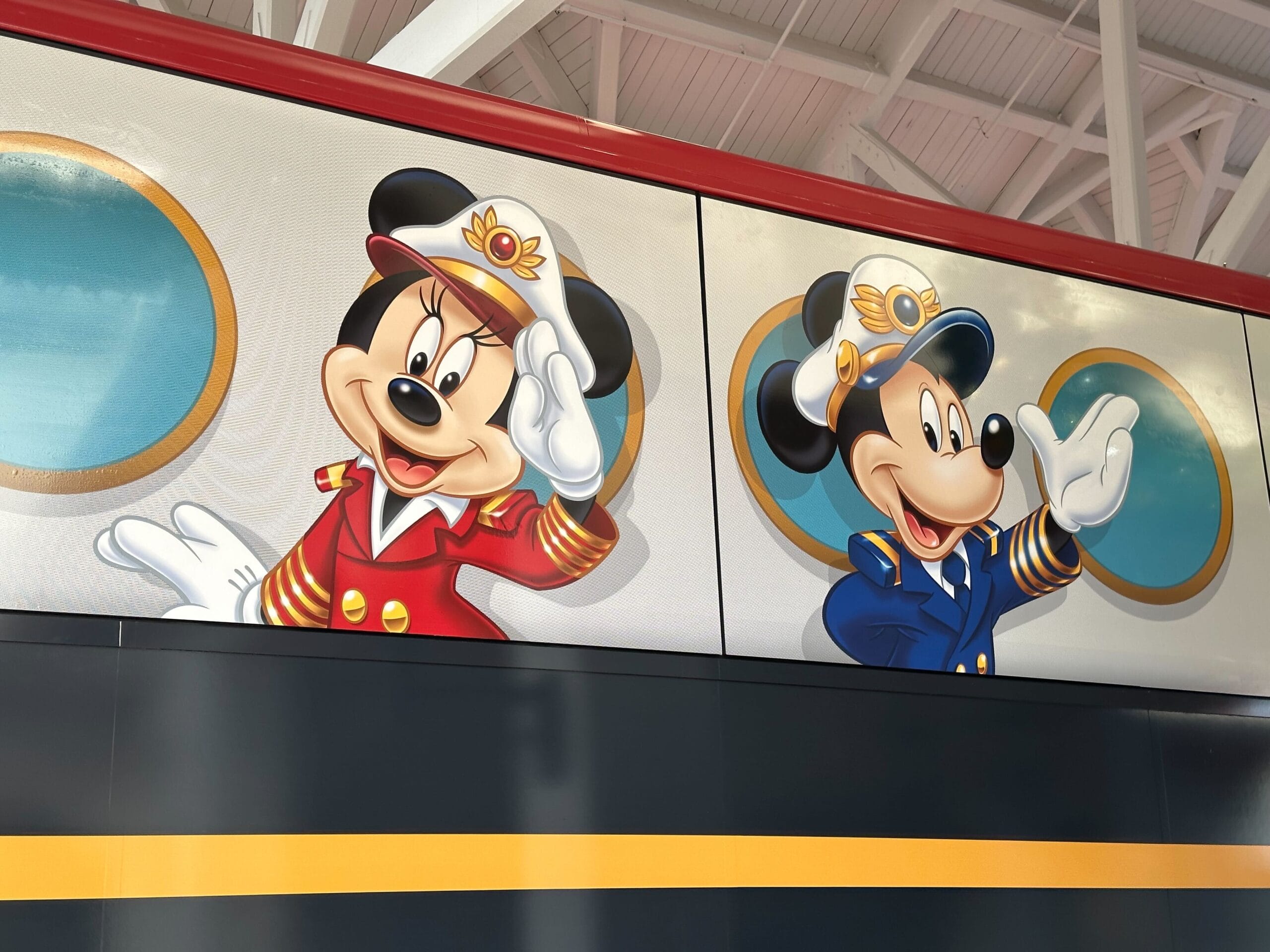 Minnie Mouse and Mickey Mouse dressed as ship captains are waving from a mural on a building wall.
