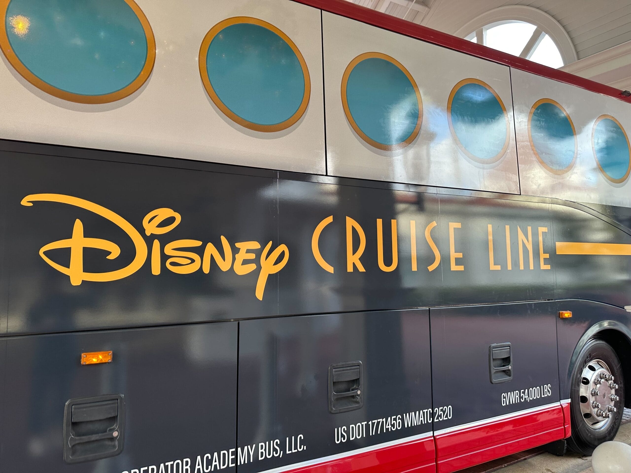 Side view of a Disney Cruise Line bus with a red and black design, featuring circular windows and white text.