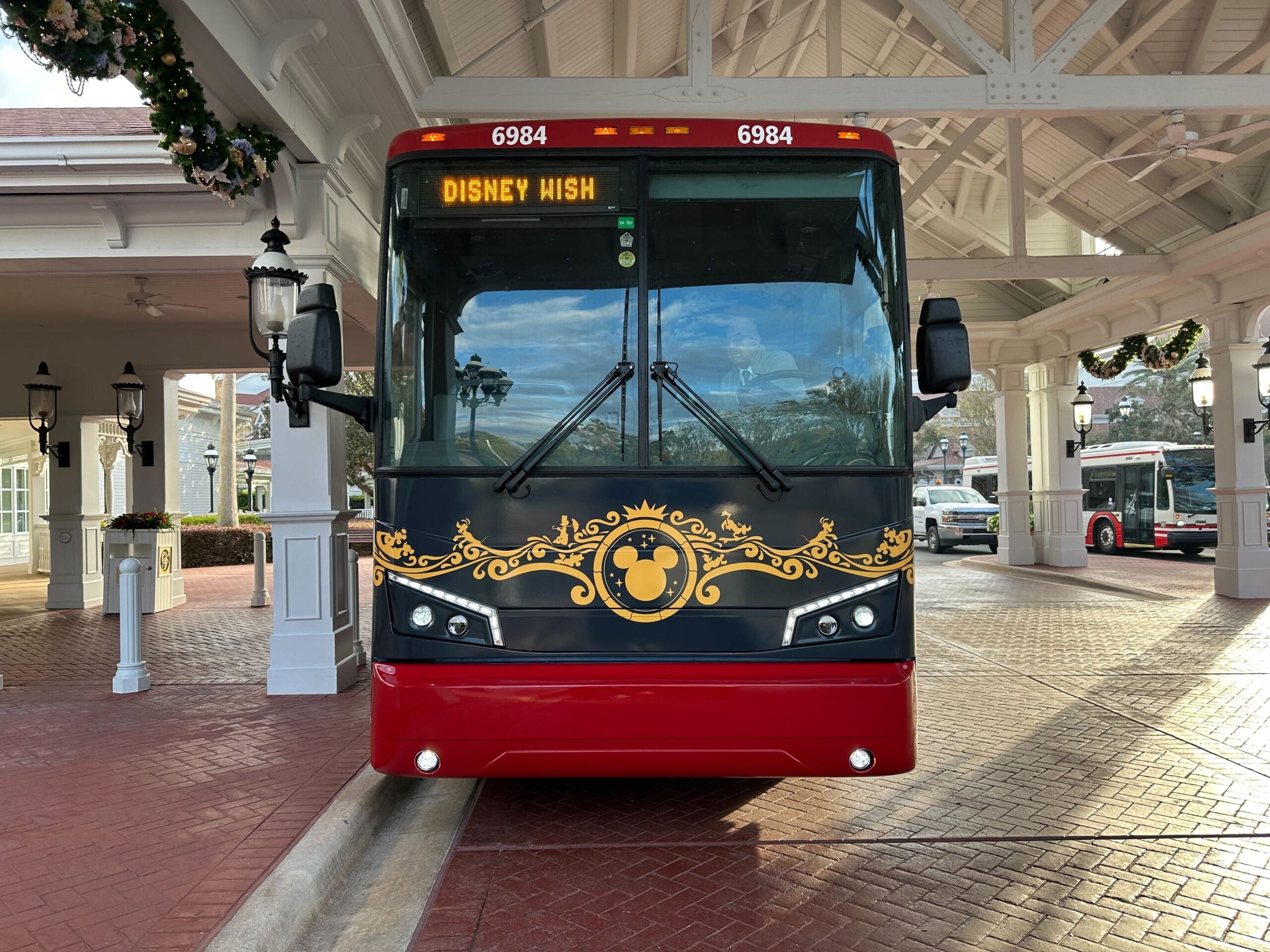 A decorated bus labeled "Disney Wish" parked under a canopy at a station with festive garlands.
