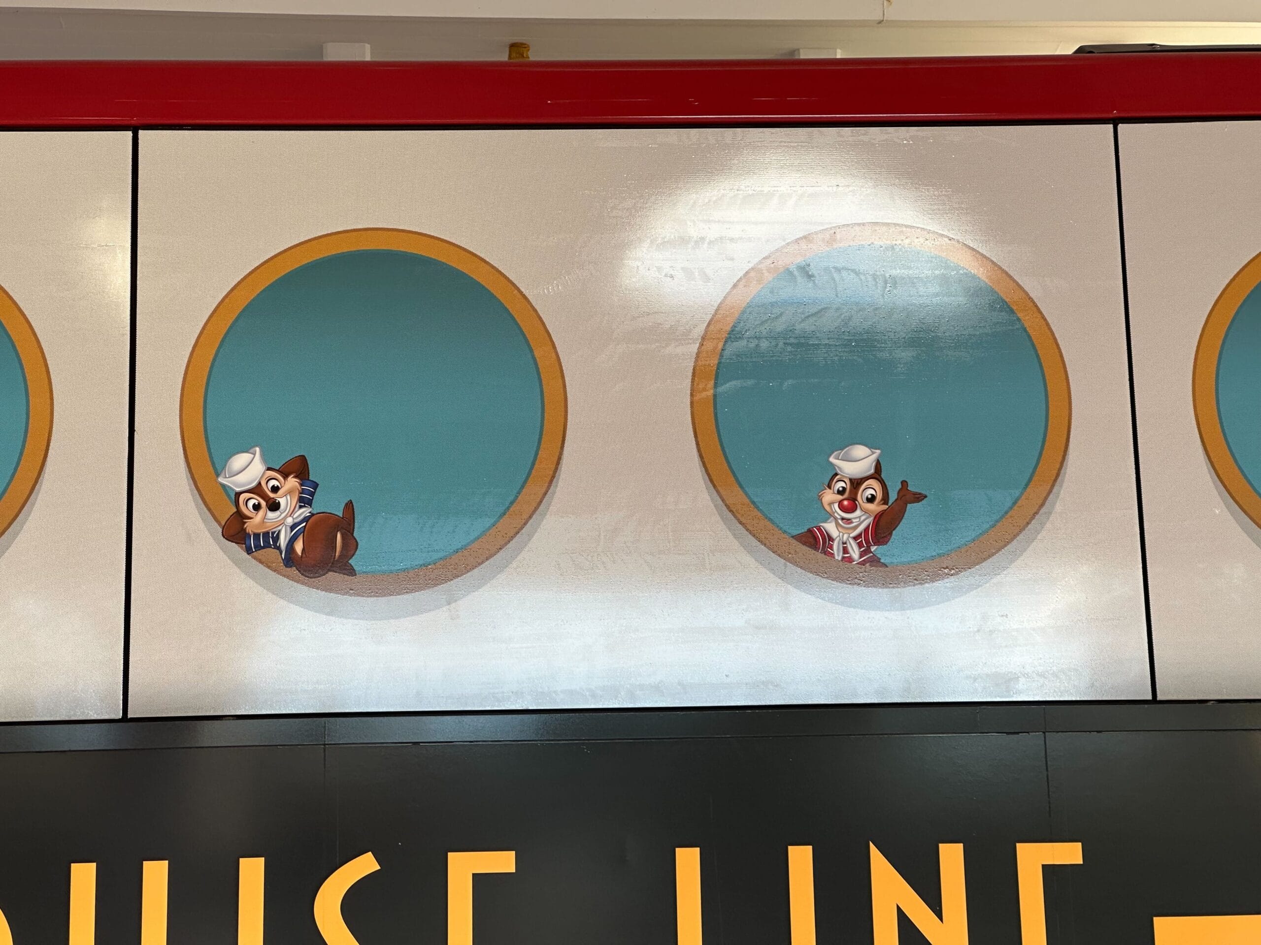 Two cartoon characters in sailor outfits, a dog and a bird, are peeking out of circular windows on a wall.