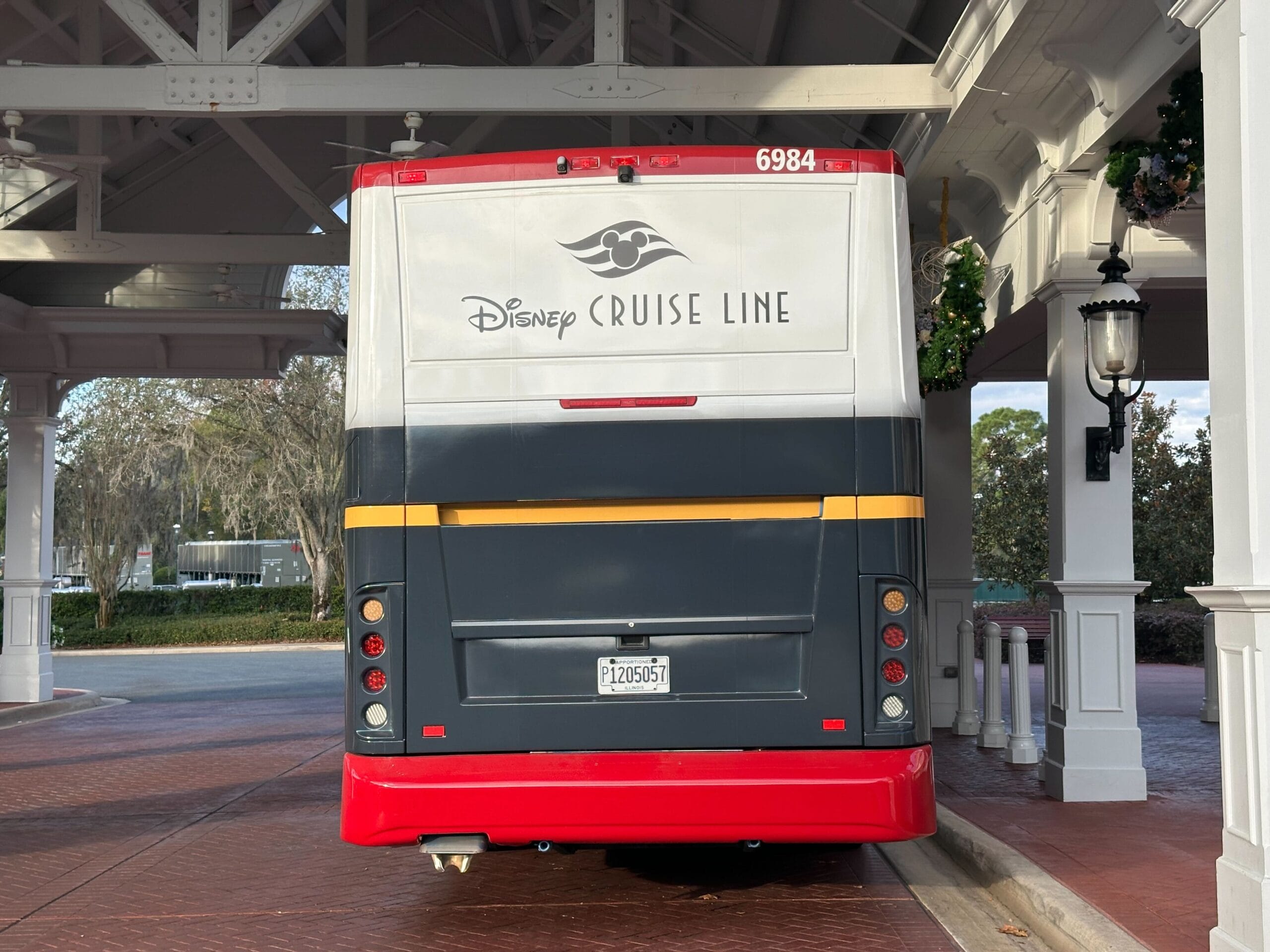The back of a Disney Cruise Line bus parked under a covered area with trees visible in the background.