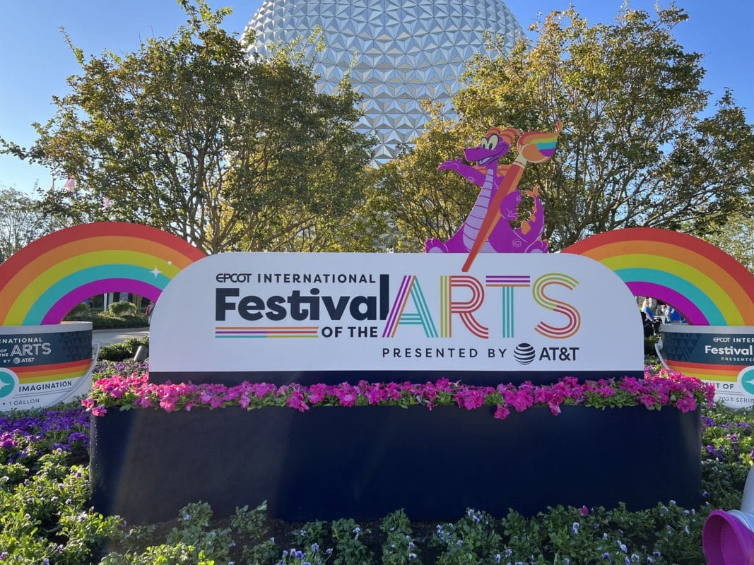 Sign for the vibrant Epcot International Festival of the Arts, featuring colorful rainbows and a lively character figure. Spaceship Earth proudly stands in the background, encapsulating a celebration of creativity and innovation.