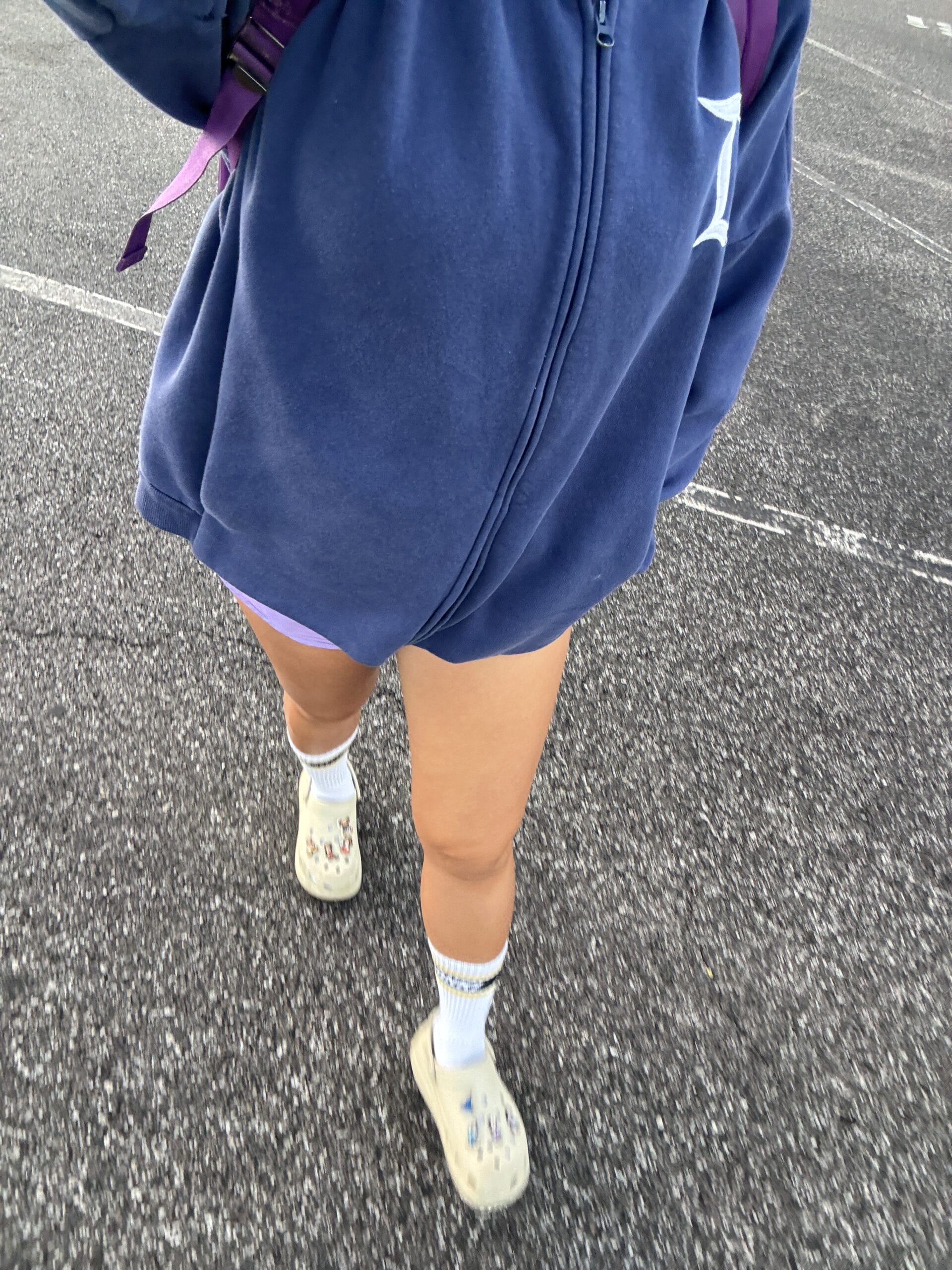 In a scene that feels straight out of a PHOTO REPORT, a person strolls down the asphalt, clad in a blue hoodie, purple shorts, socks, and Crocs, with a backpack. You might almost imagine they're heading to the Magic Kingdom for an enchanting day ahead.