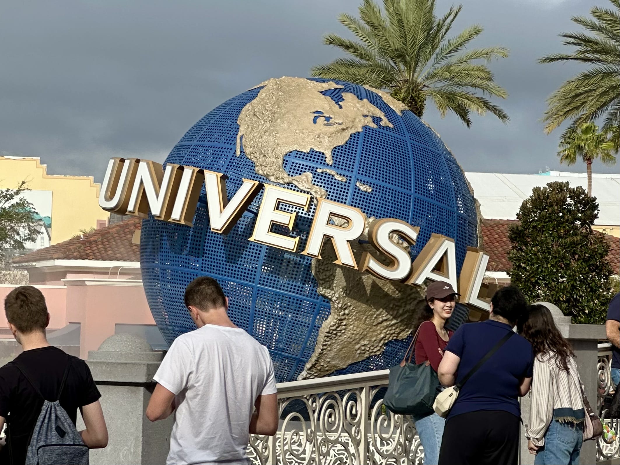 People stand near the large globe structure with "Universal" text at Universal Studios. Palm trees and buildings are in the background.