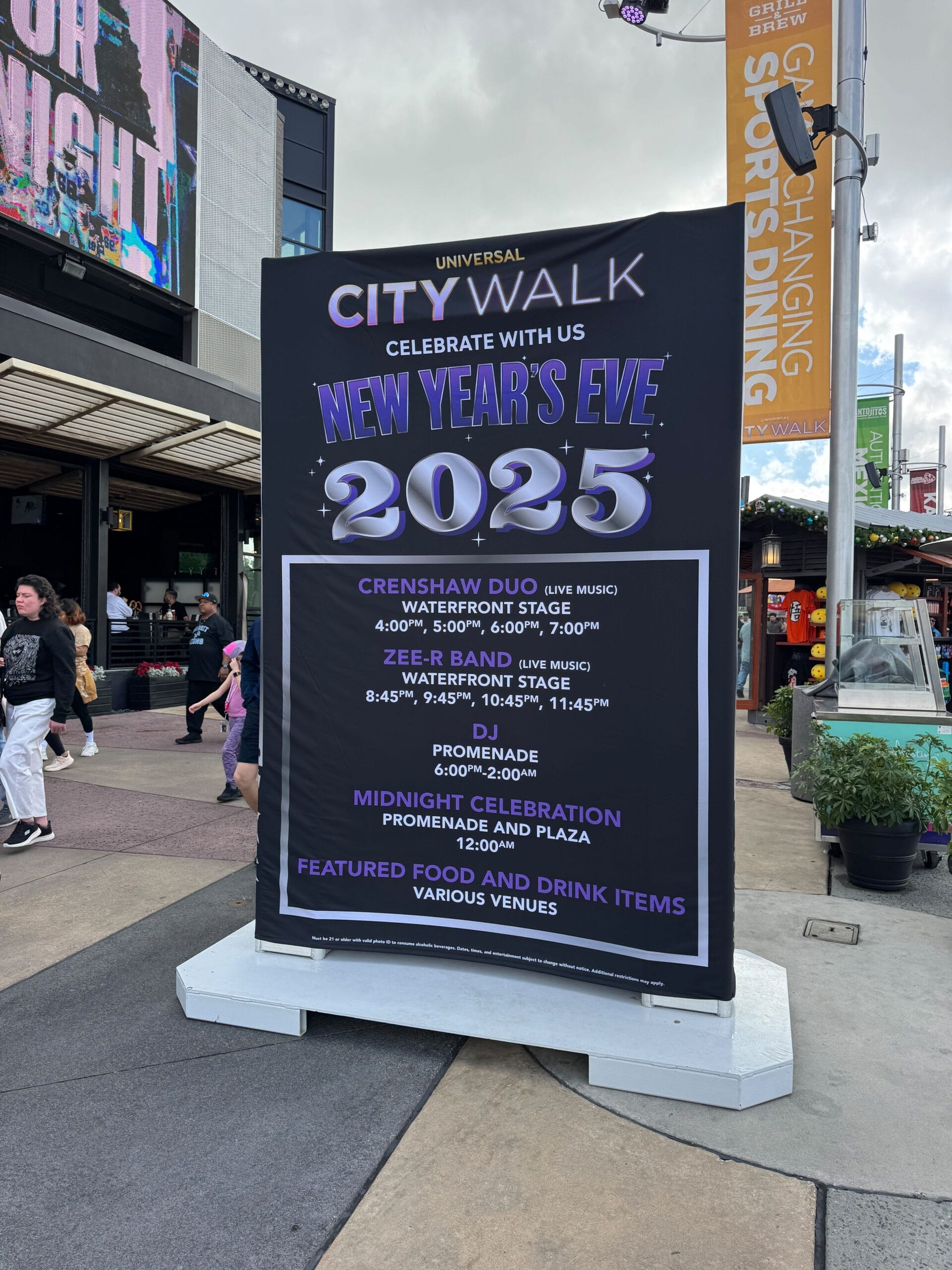 Sign promoting New Year's Eve 2025 at Universal CityWalk, featuring live music, food, and drink from 6 PM with performances by Crenshaw Duo and Zee R. Band.