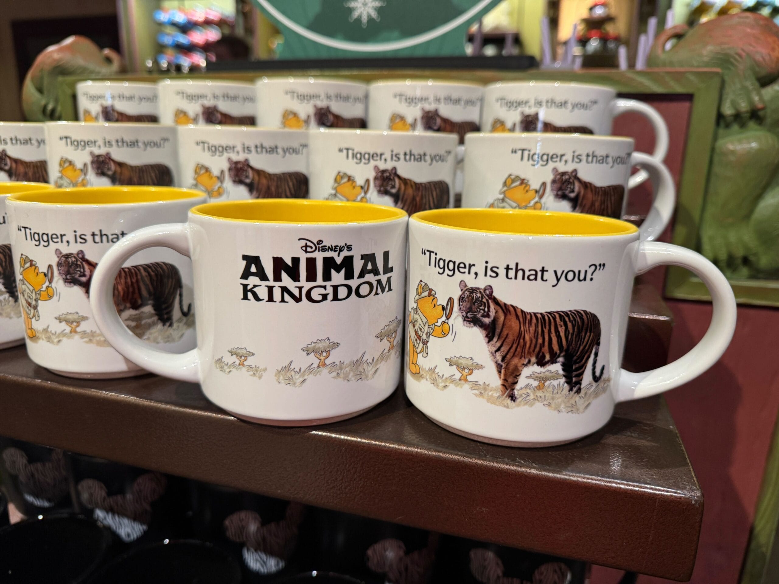 White mugs on a shelf featuring a cartoon tiger, the text "Disney's Animal Kingdom," and the phrase "Tigger, is that you?" bring a whimsical touch to your collection. Perfect for fans of Winnie the Pooh!.