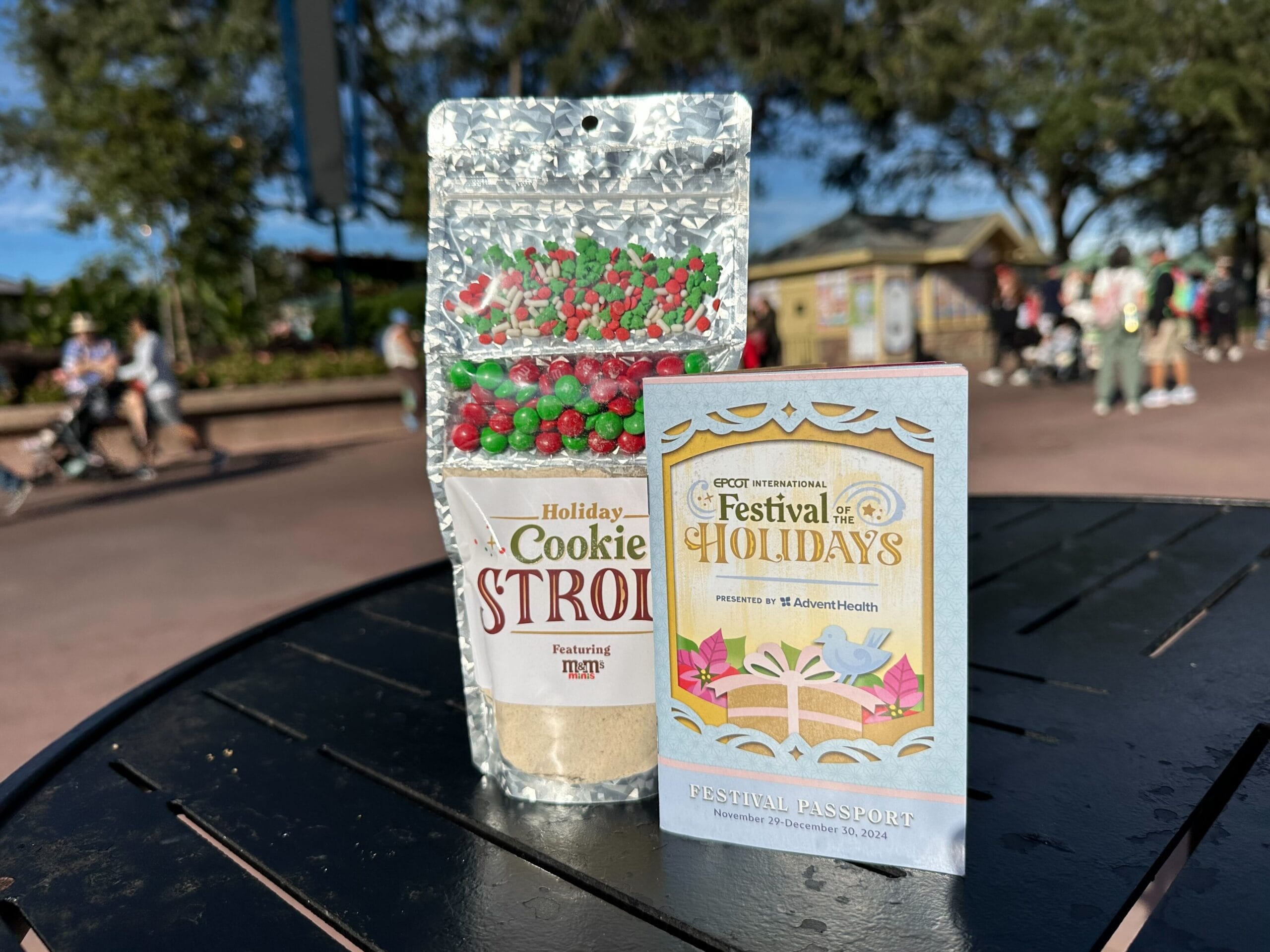 A package of Holiday Cookie Stroll delights, featuring M&M's, sits on a table alongside a Festival of Holidays passport booklet.