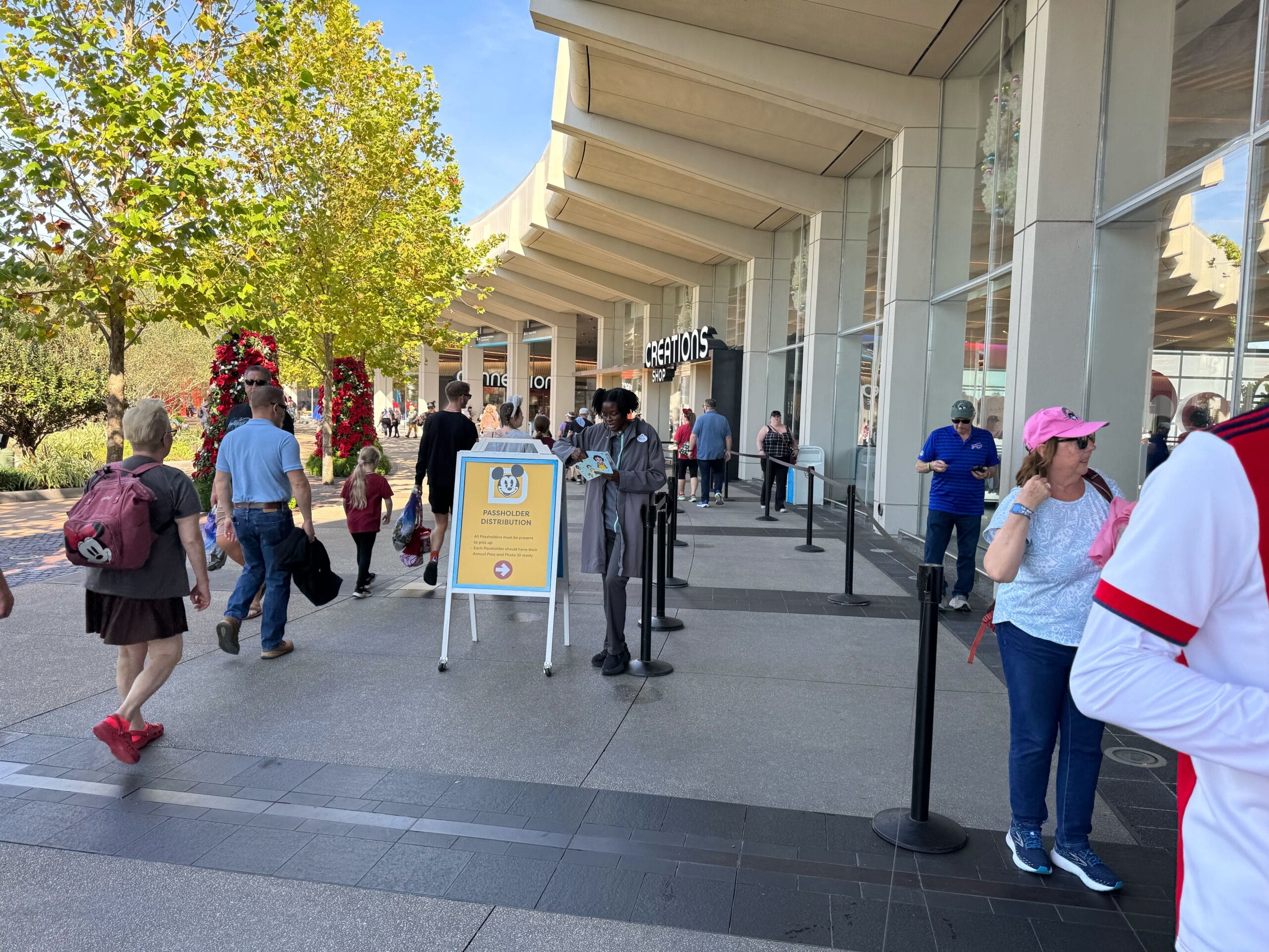 People are walking outside a shopping center. A sign reads "Santa Experience Entrance." Some, flashing their Annual Passholder badges, are in line for seasonal joys, while others stroll past, embracing the holiday spirit.