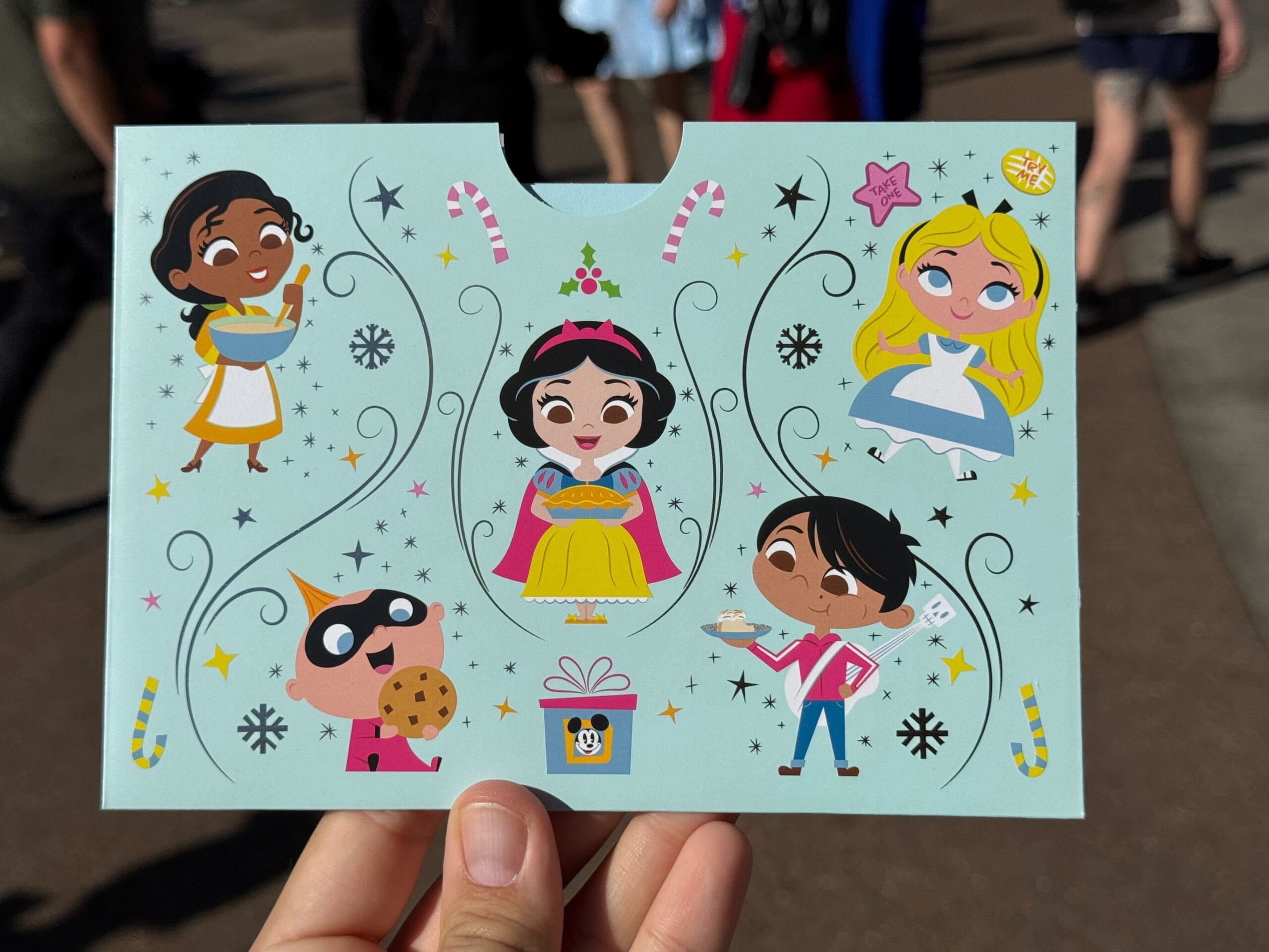 Cartoon characters on a greeting card, featuring a princess with a pie recipe card, surrounded by a diverse group of kids, decorative elements, and a gift box.