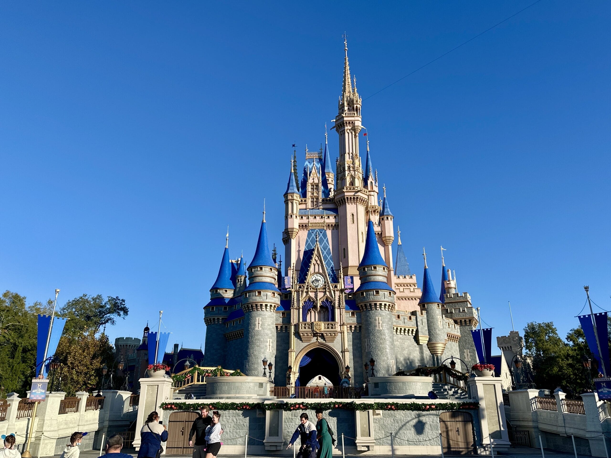 A large castle with blue spires under a clear blue sky, surrounded by people walking and taking photos.
