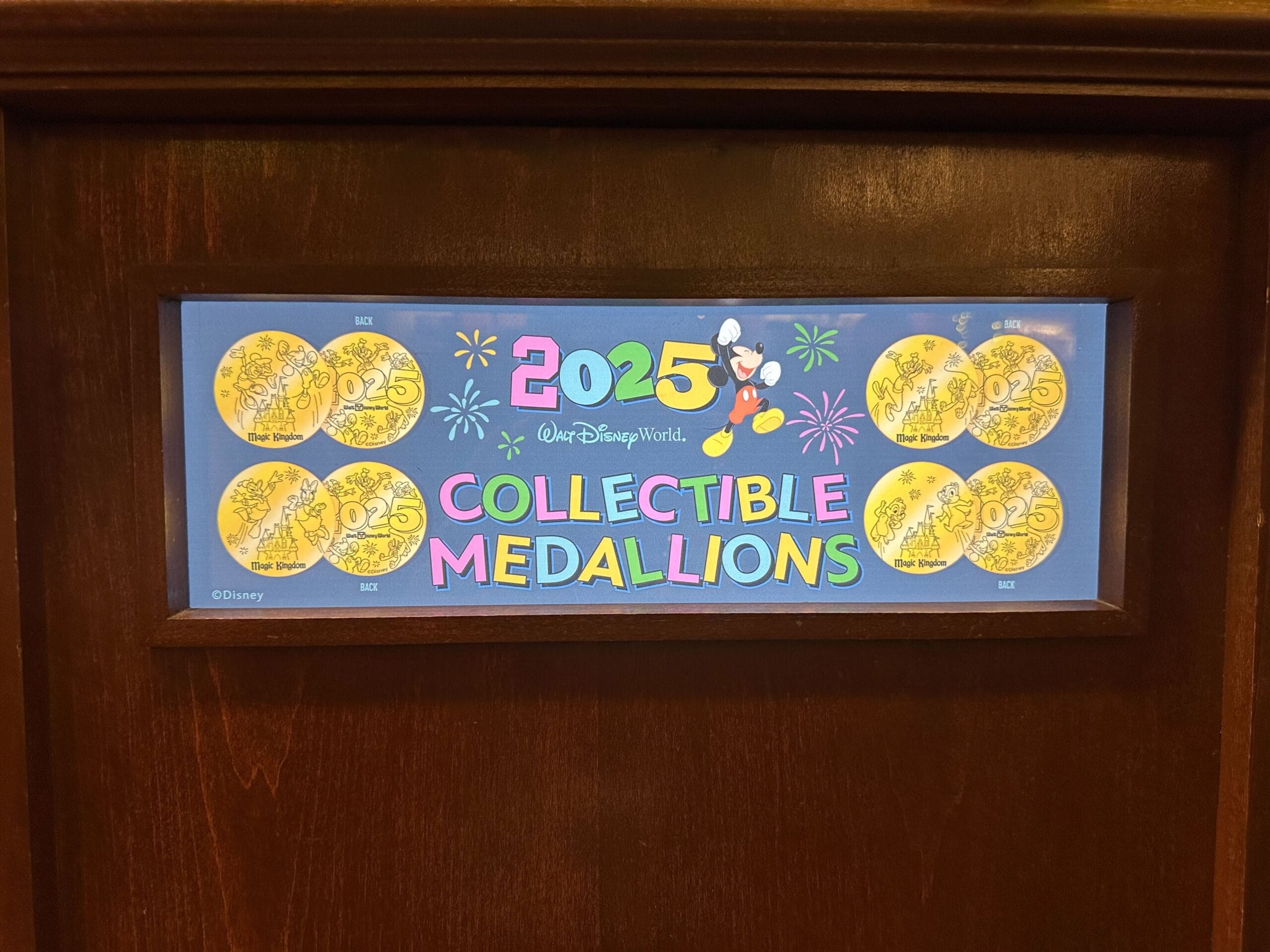 Display case featuring Disney World collectible medallions for 2025, with Mickey Mouse graphic and fireworks design.