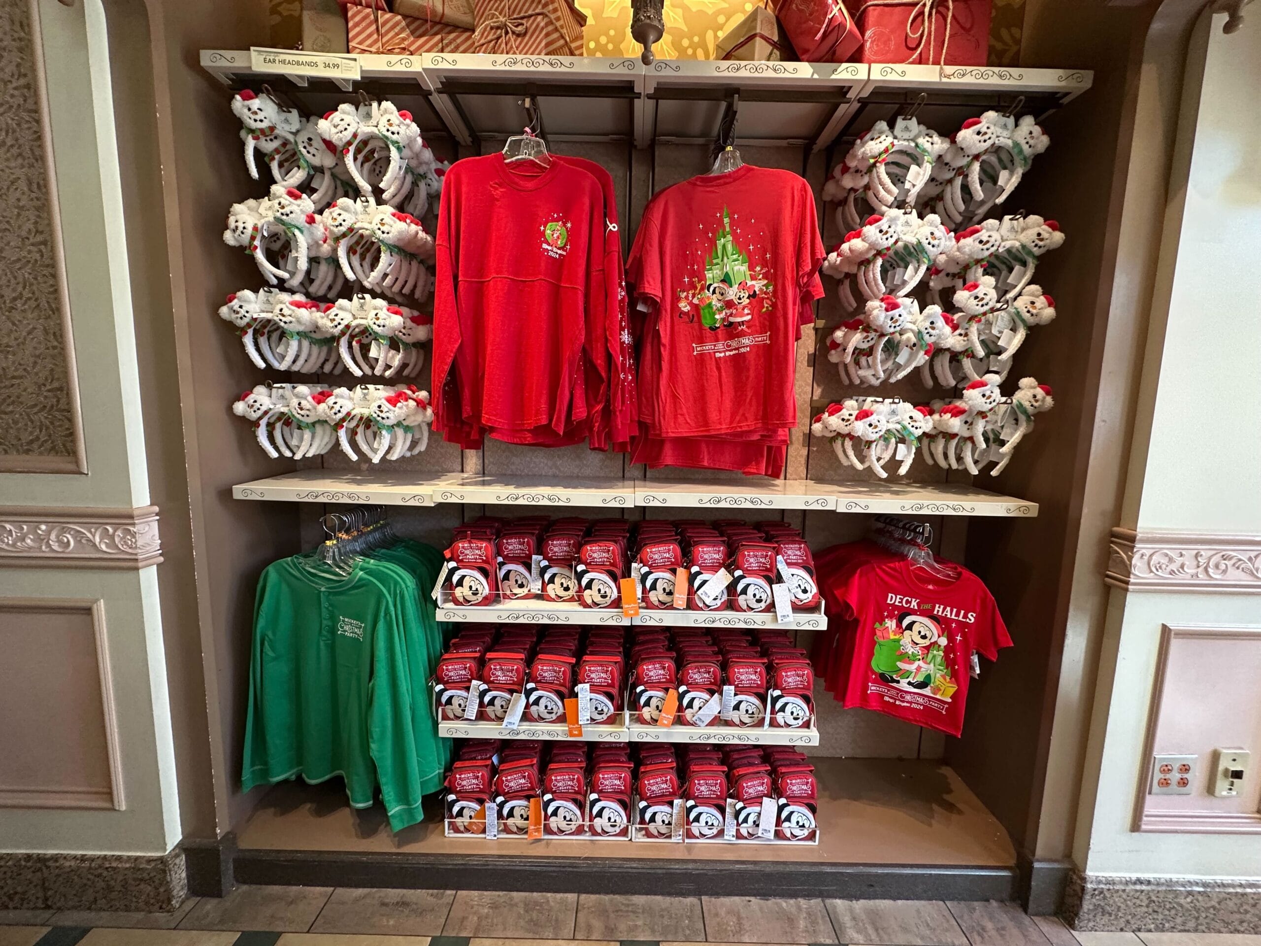 Merchandise display with red and green holiday shirts, surrounded by plush toy headbands and themed mugs on shelves.