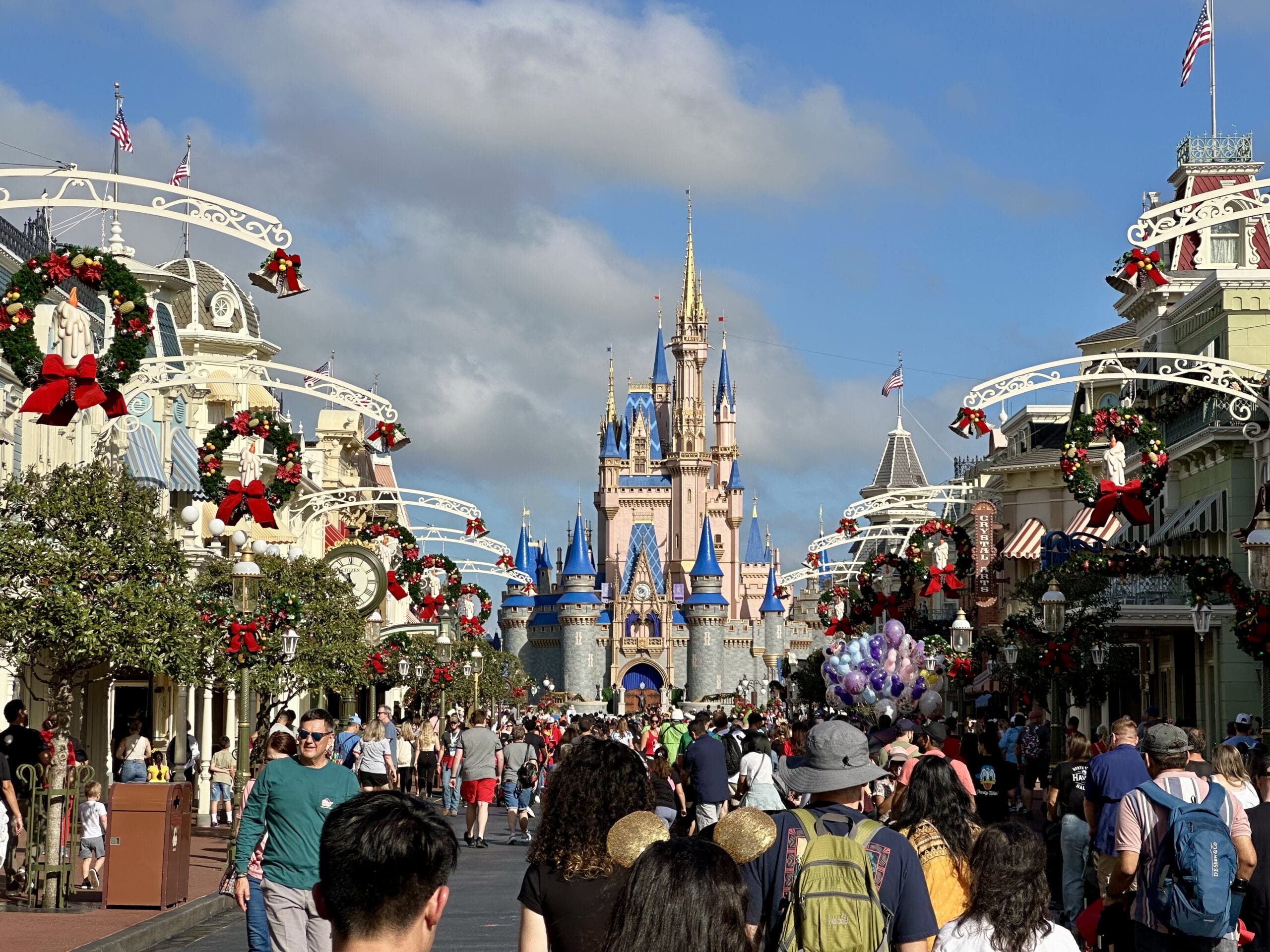Crowded street leading to a castle decorated for the holidays, with festive wreaths and bows.