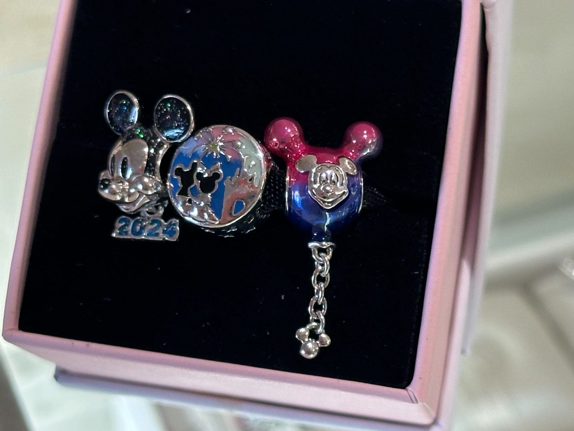 Two Disney-themed pins in a box: one with Mickey ears, "2023," and star designs; the other with a pink Mickey ear and face, connected by a chain.