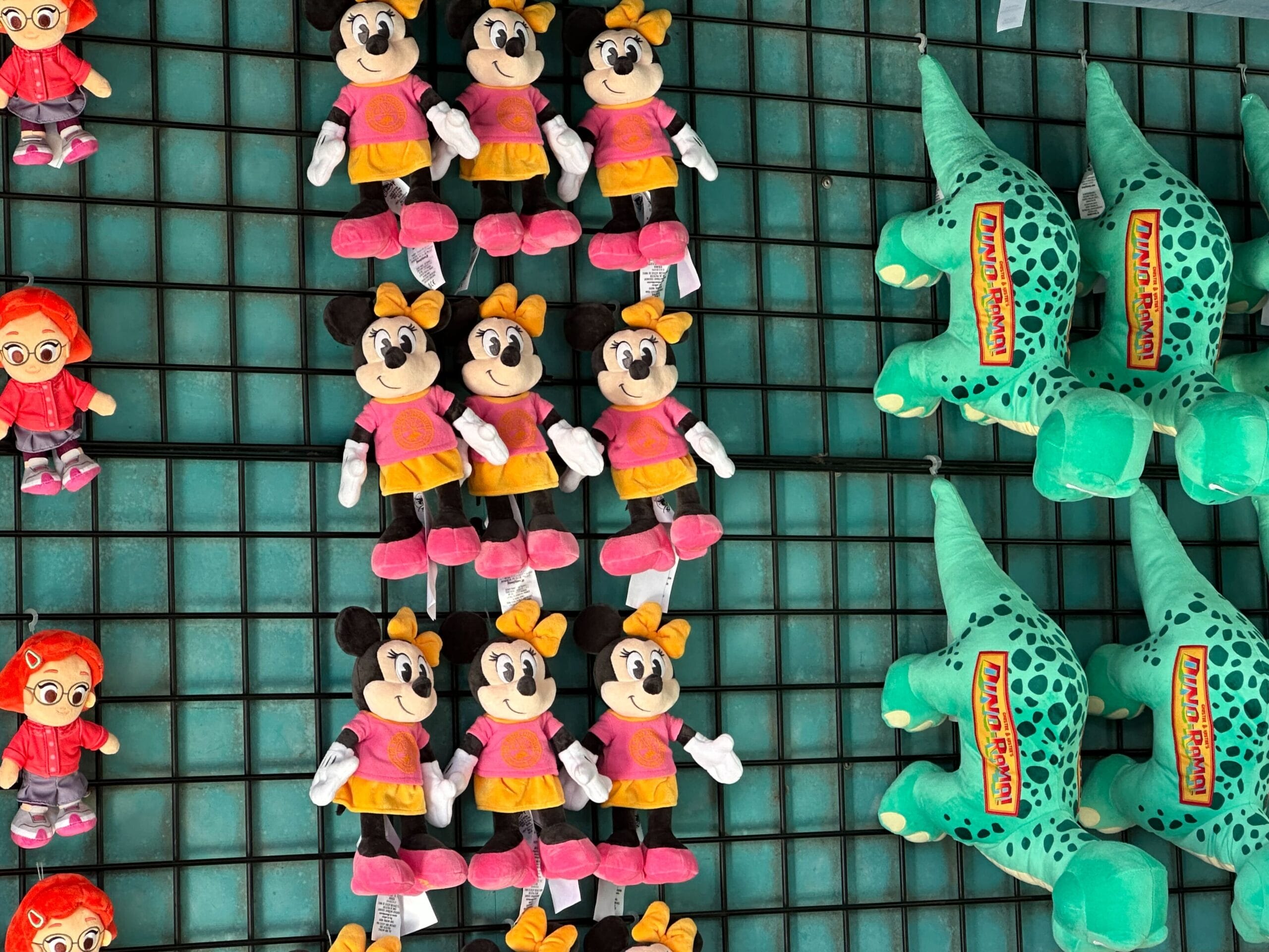 Plush toys hang on a grid display, showcasing charming Wishables with cartoon mice in pink outfits and playful green dinosaurs, reminiscent of the fun at DinoLand Carnival Games.