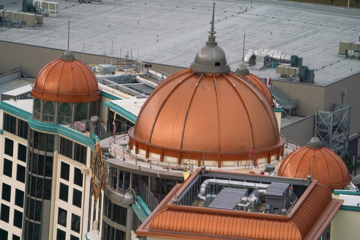 Aerial view of a building with multiple copper domes and a rooftop adorned with industrial equipment, reminiscent of an Epic Universe setting.